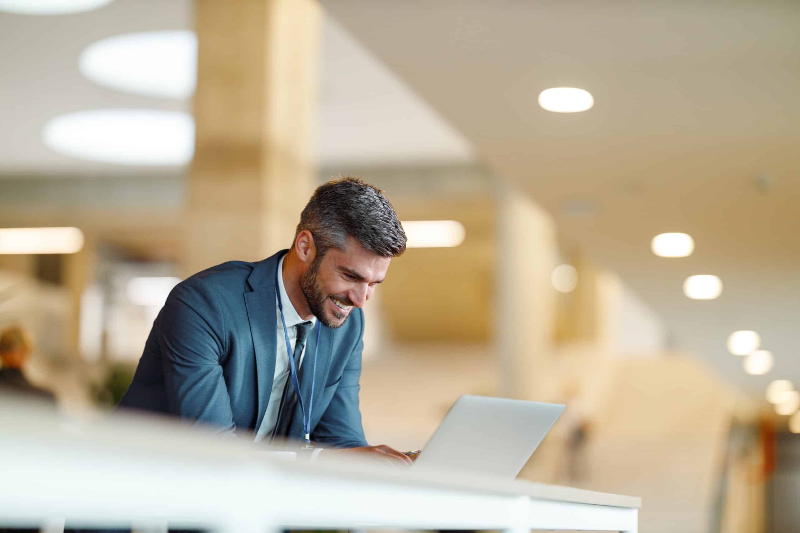 Smiling man in a suit working on a laptop at a Geospatial Analytics Consulting firm.
