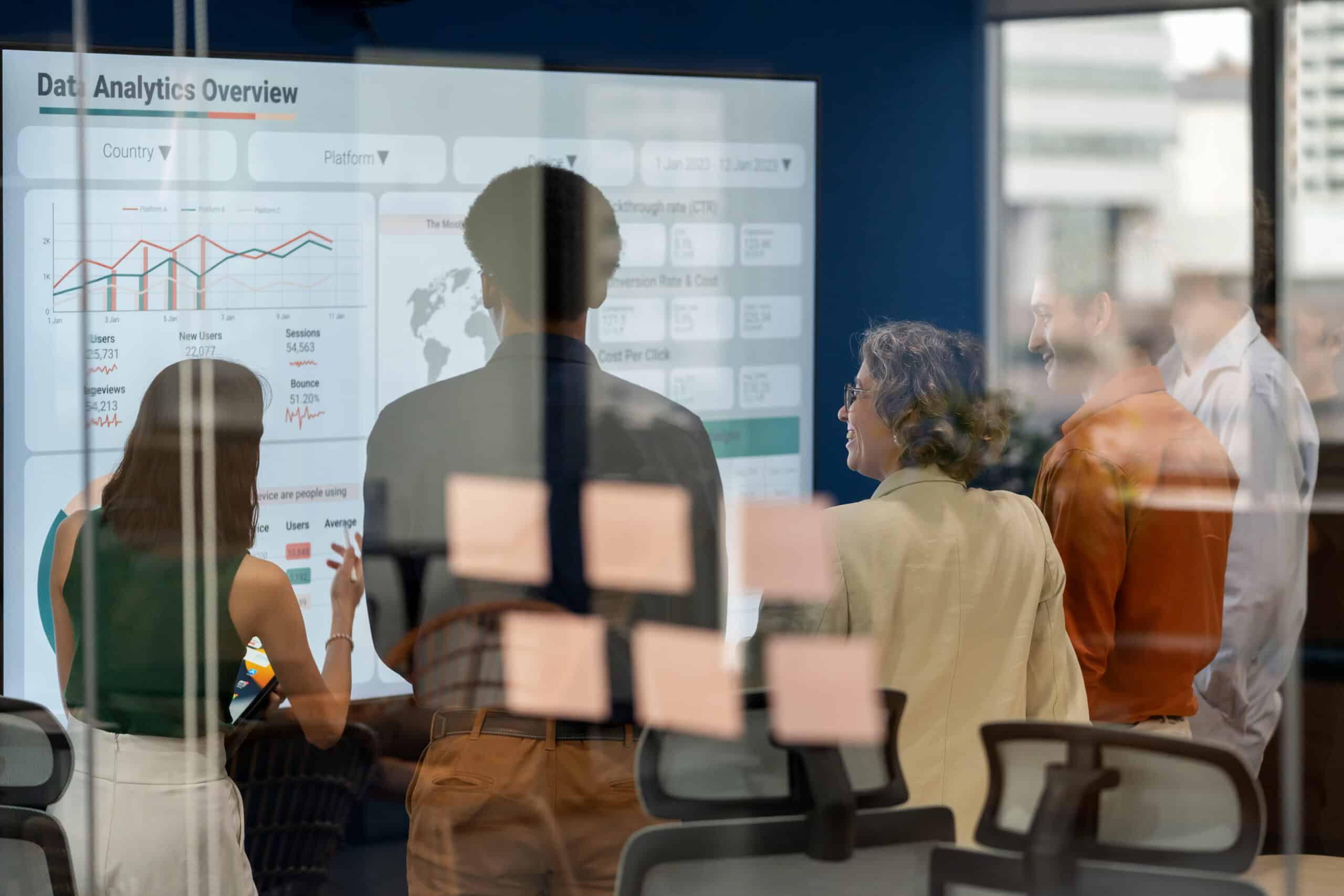 Four people stand before a large screen showcasing demand forecasting analytics and graphs.