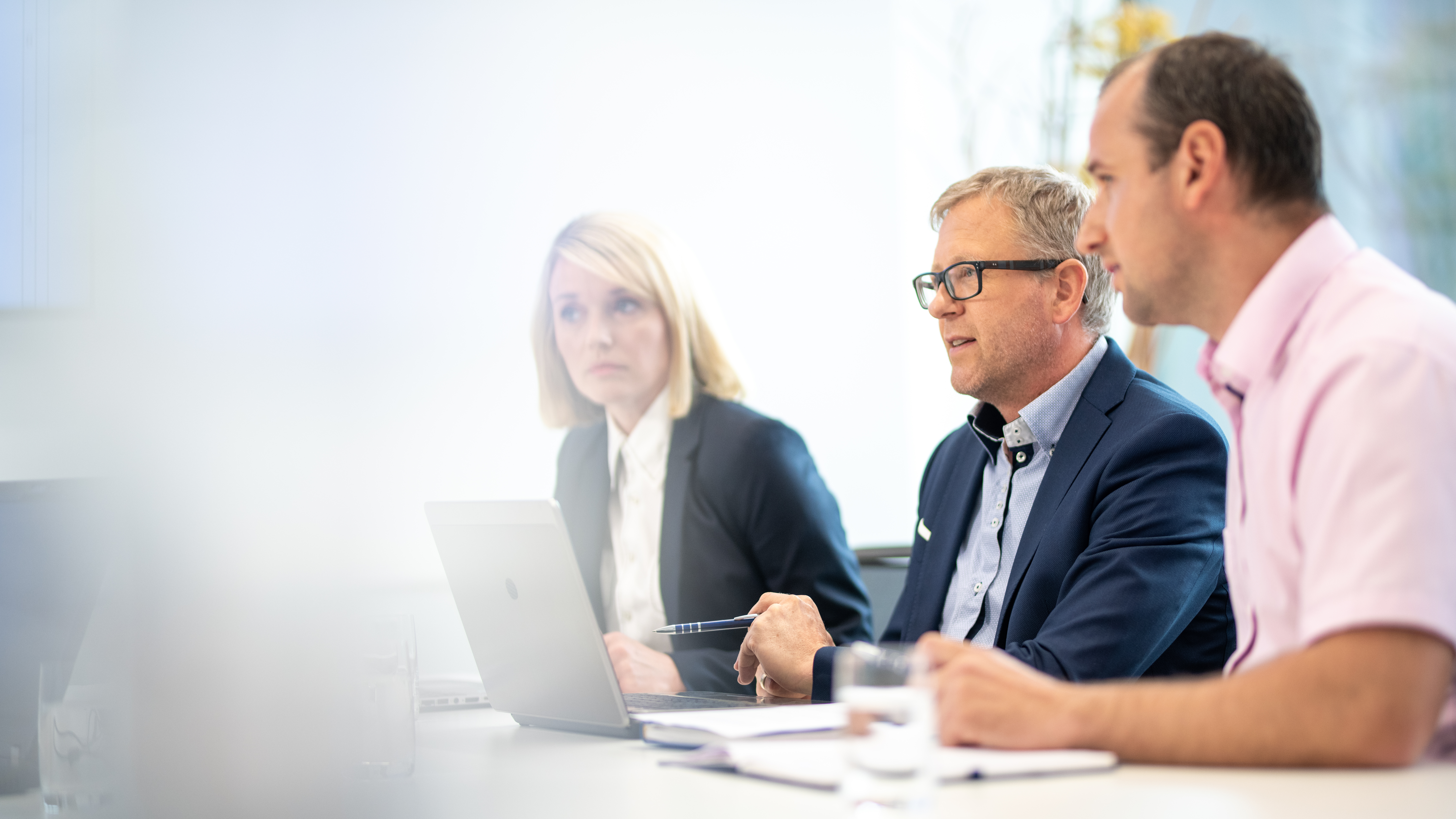 Three professionals discuss CRE Change Management at a table with laptops and notebooks.