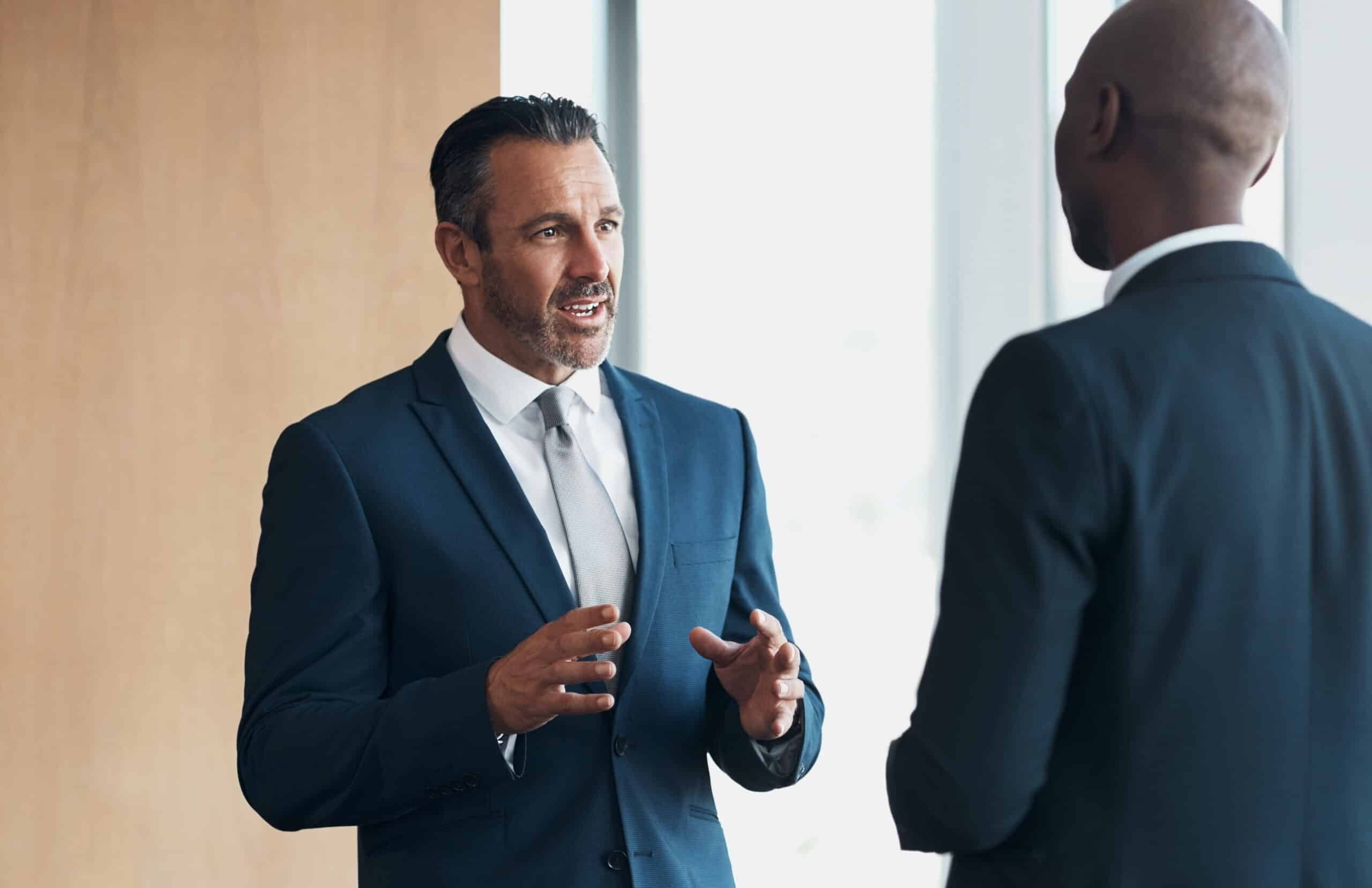 Two men in suits having a conversation in a modern office setting.