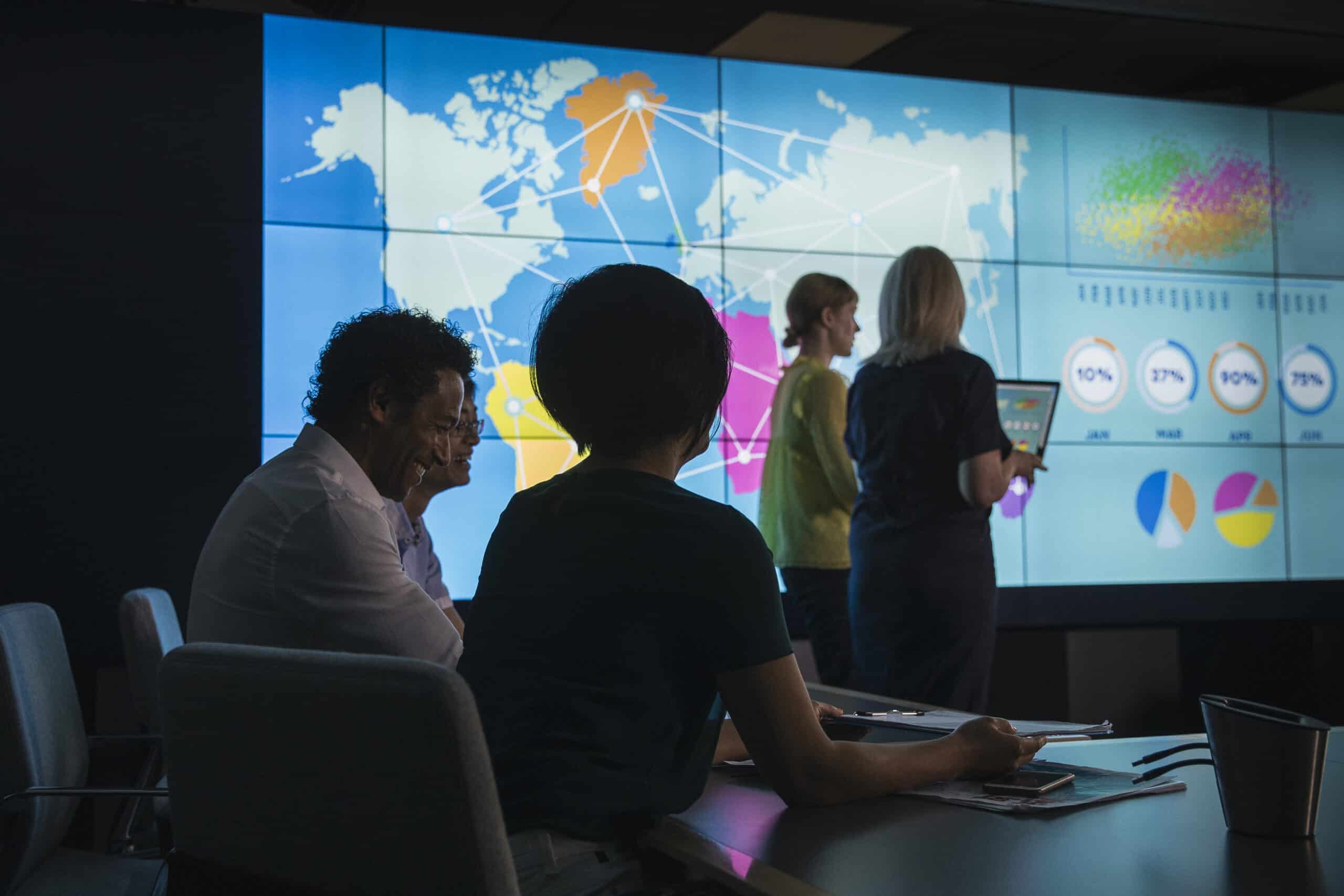 People analyzing data with Location Intelligence on a large screen in a meeting room.