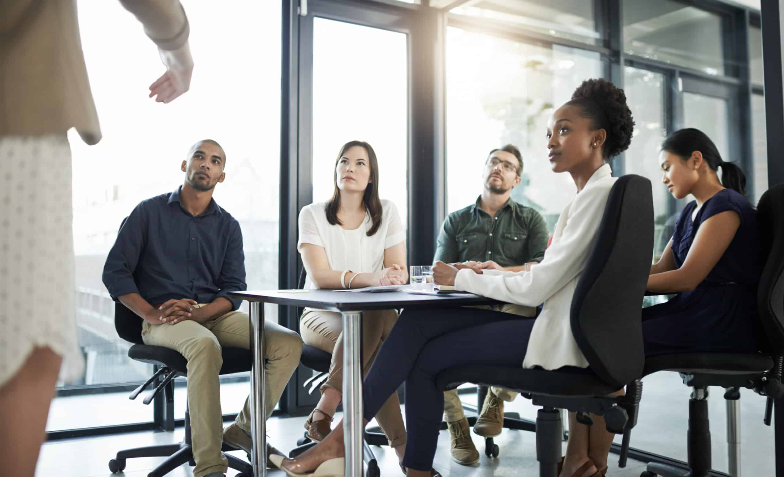 Five people seated at a table discuss CRE Workplace Strategy with a standing speaker.