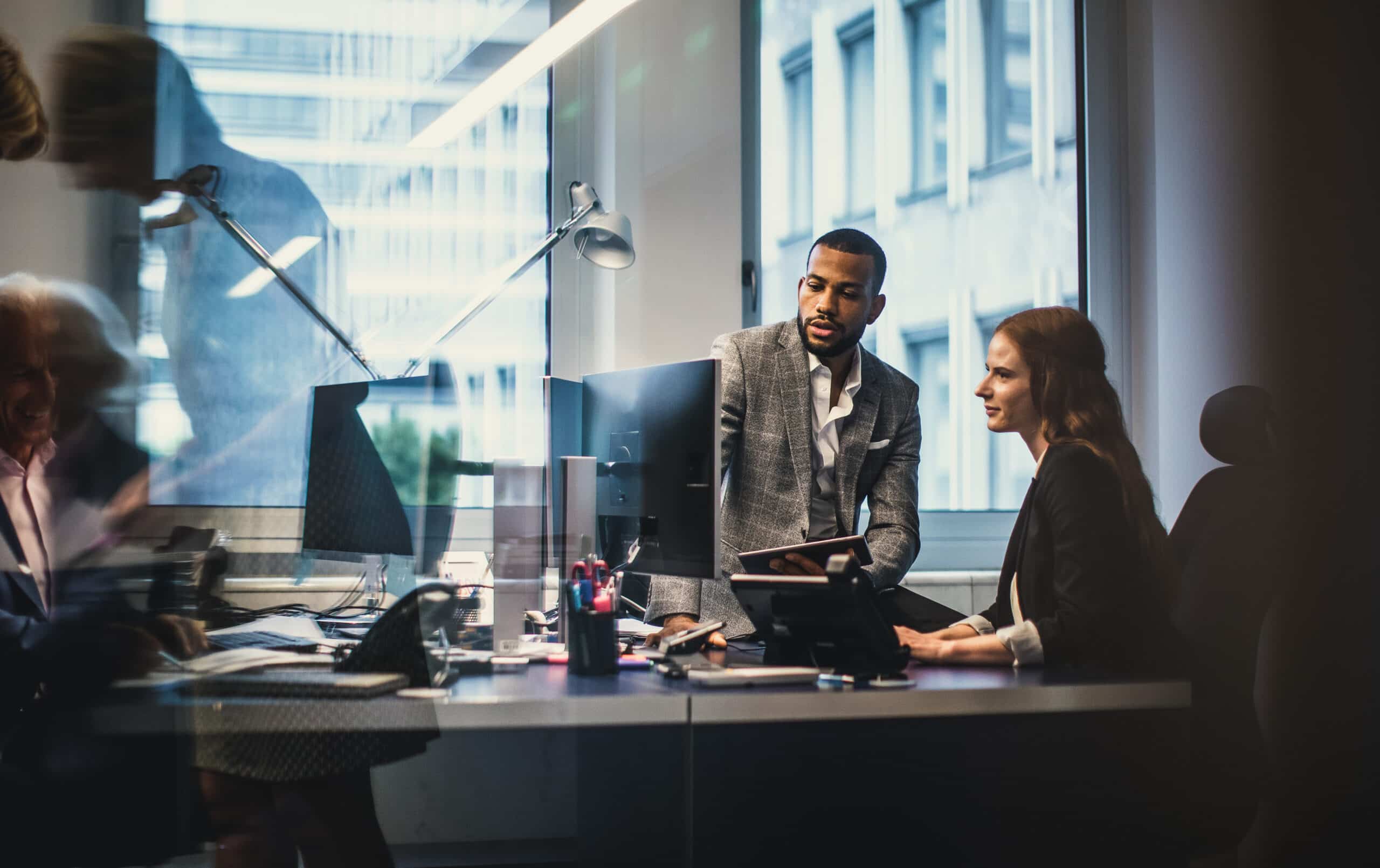 Two colleagues discuss Geospatial Analytics Consulting at a desk in a modern, bright office.