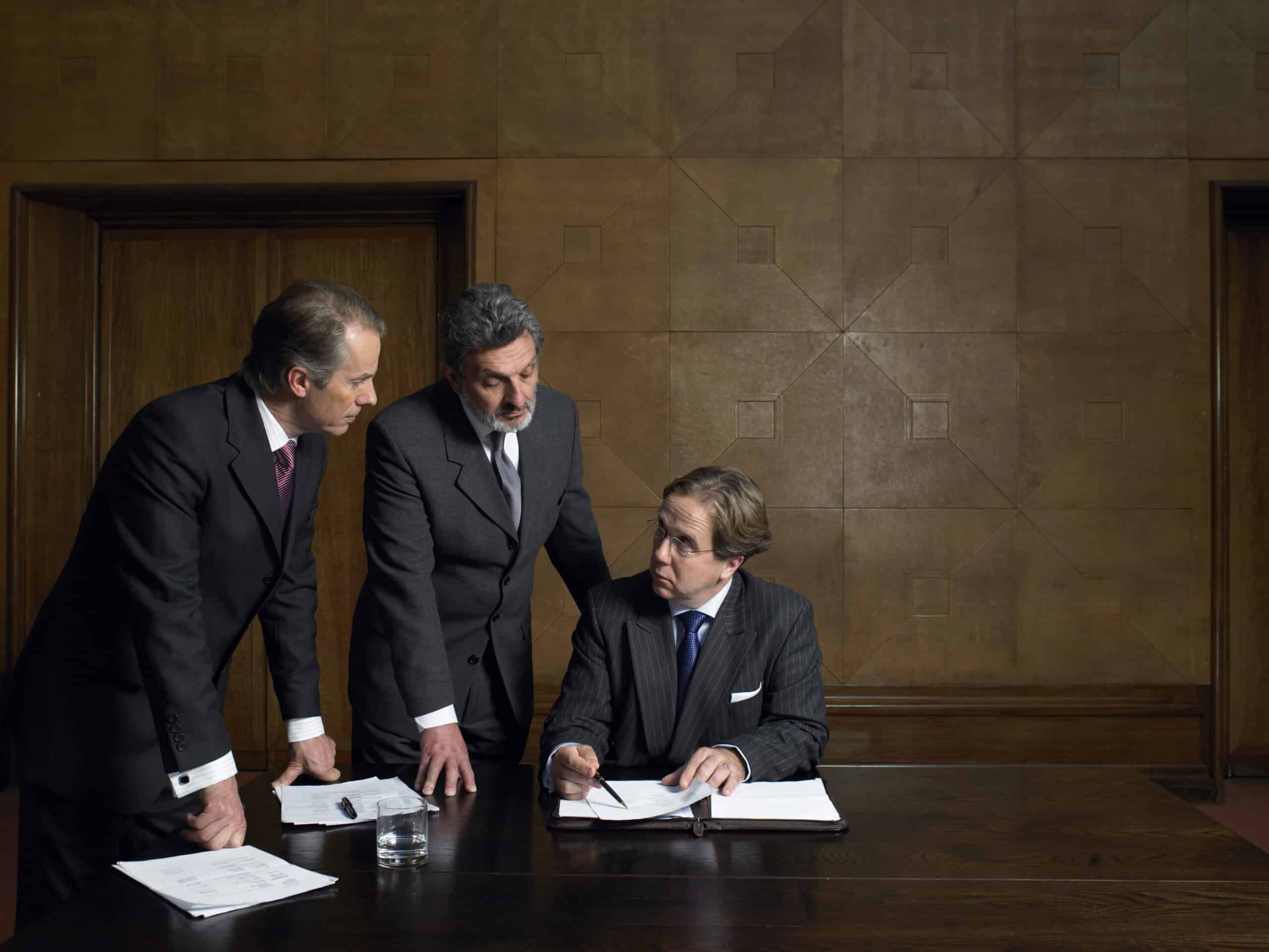 Three businessmen discuss documents, focusing on Expert Witness Services Consulting in the office.