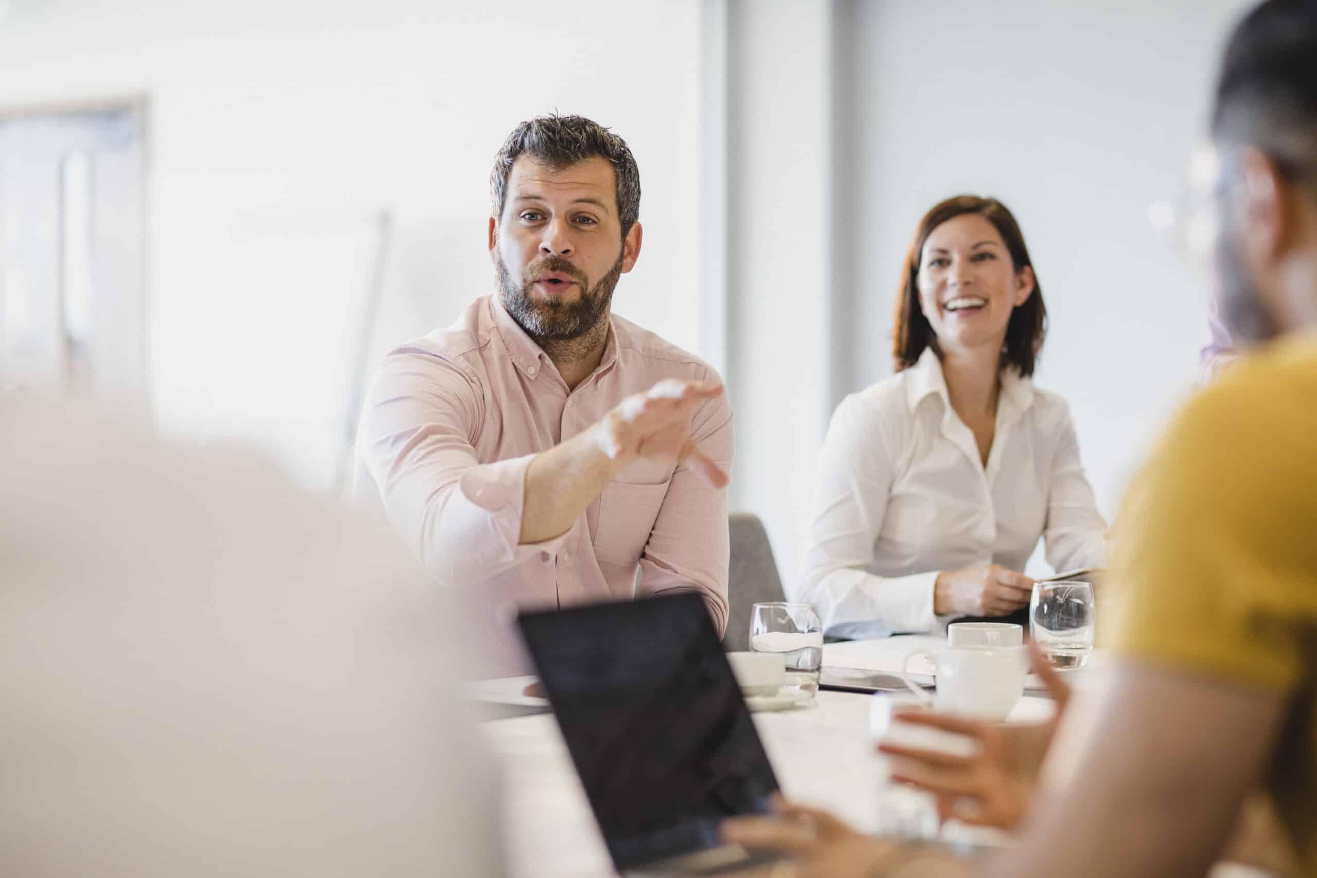 Man discussing AI Governance in a meeting, colleagues listening and smiling around a table.