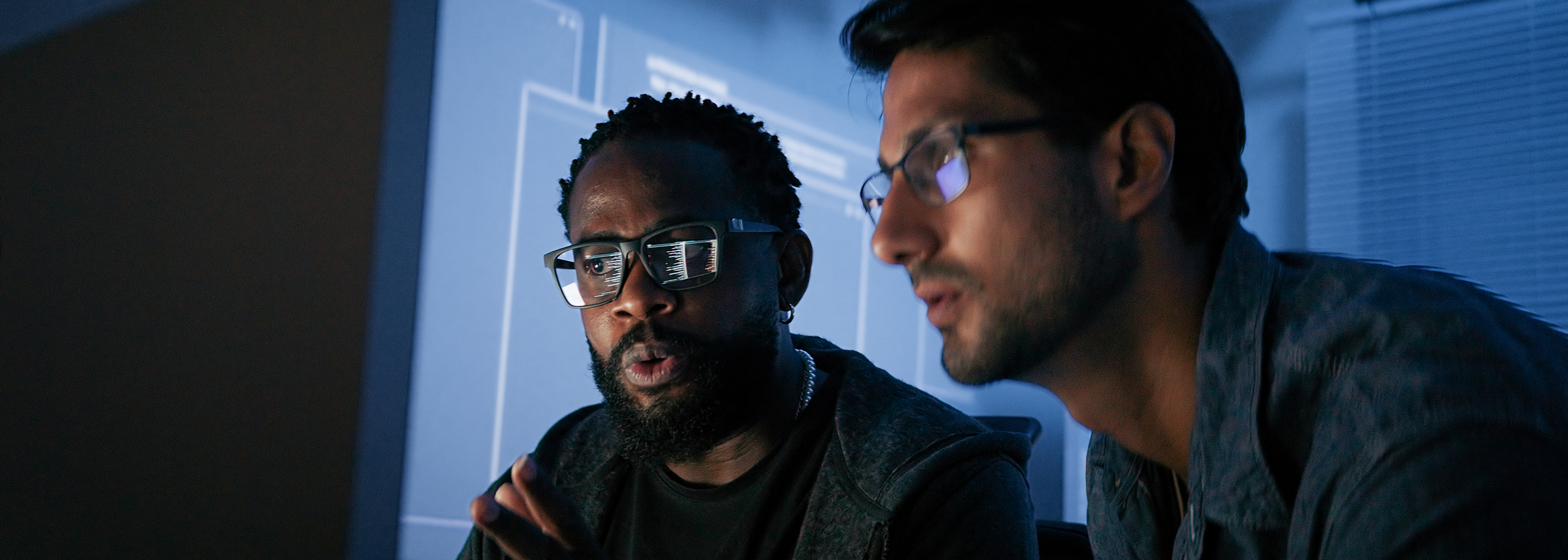 Two men wearing glasses work intently at a computer, deep in IT Architecture consulting.