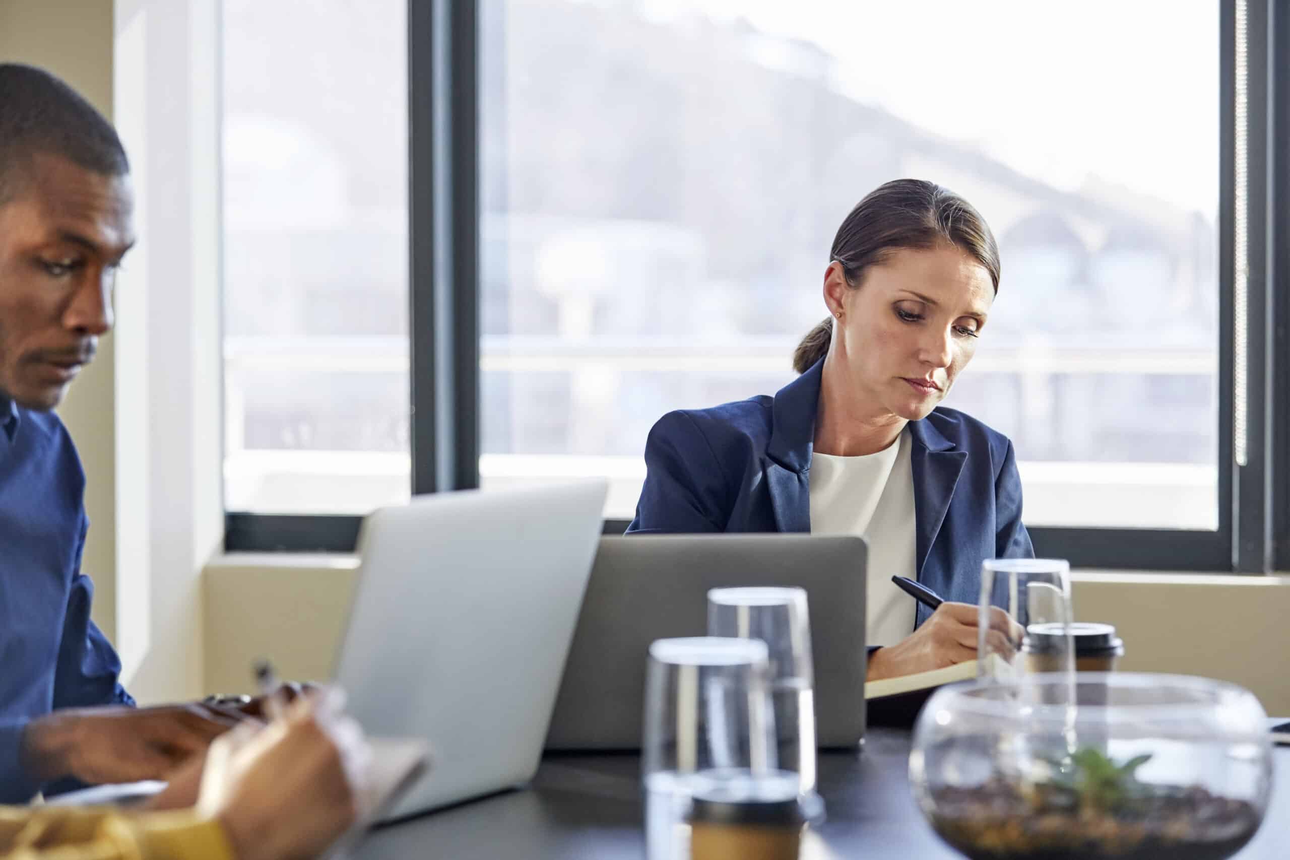 Two IoT Consultants working at a table with laptops and notebooks in a bright office setting.