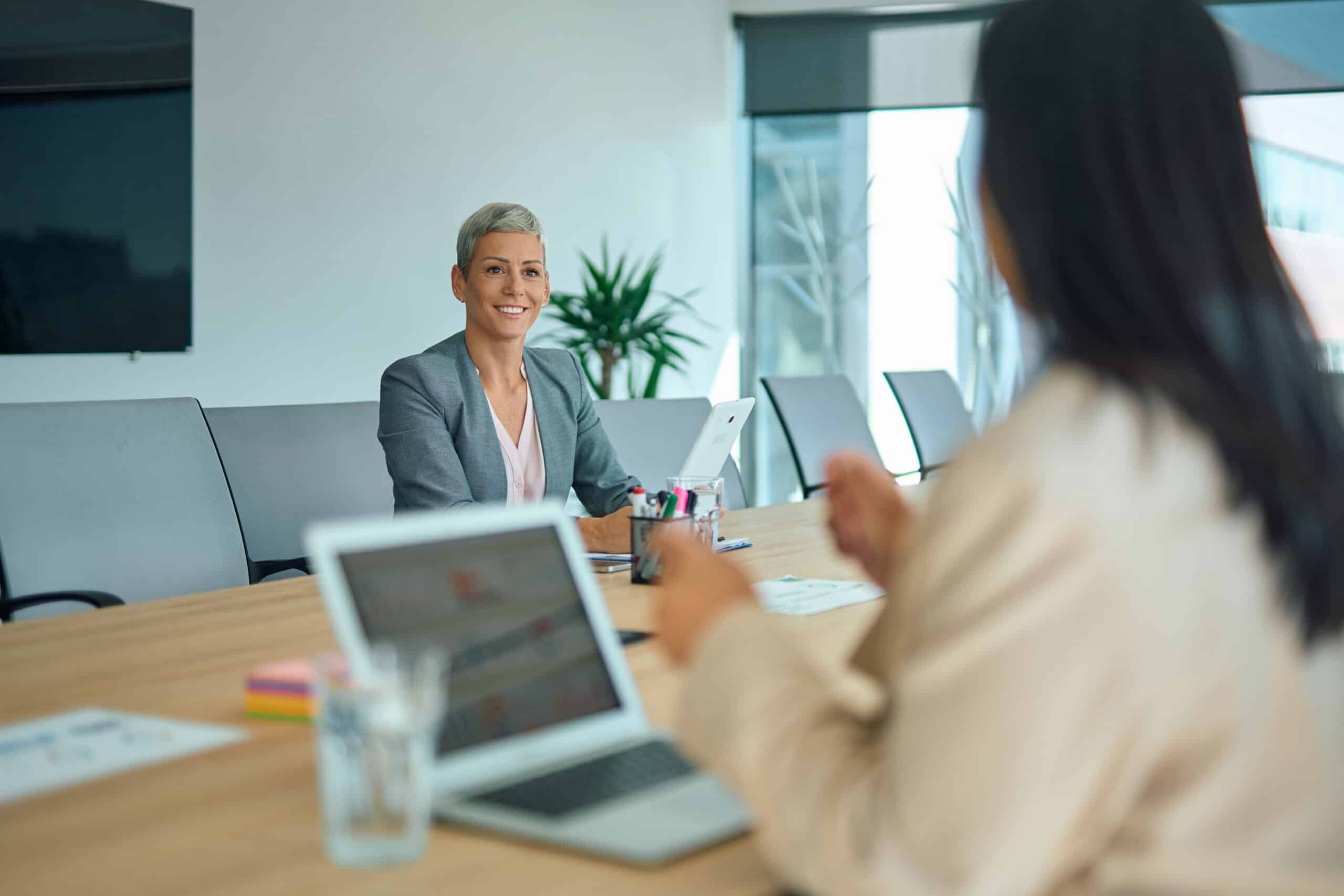 Two women in a modern office discuss Commercial Lease Dispute Resolution​ with laptops open.