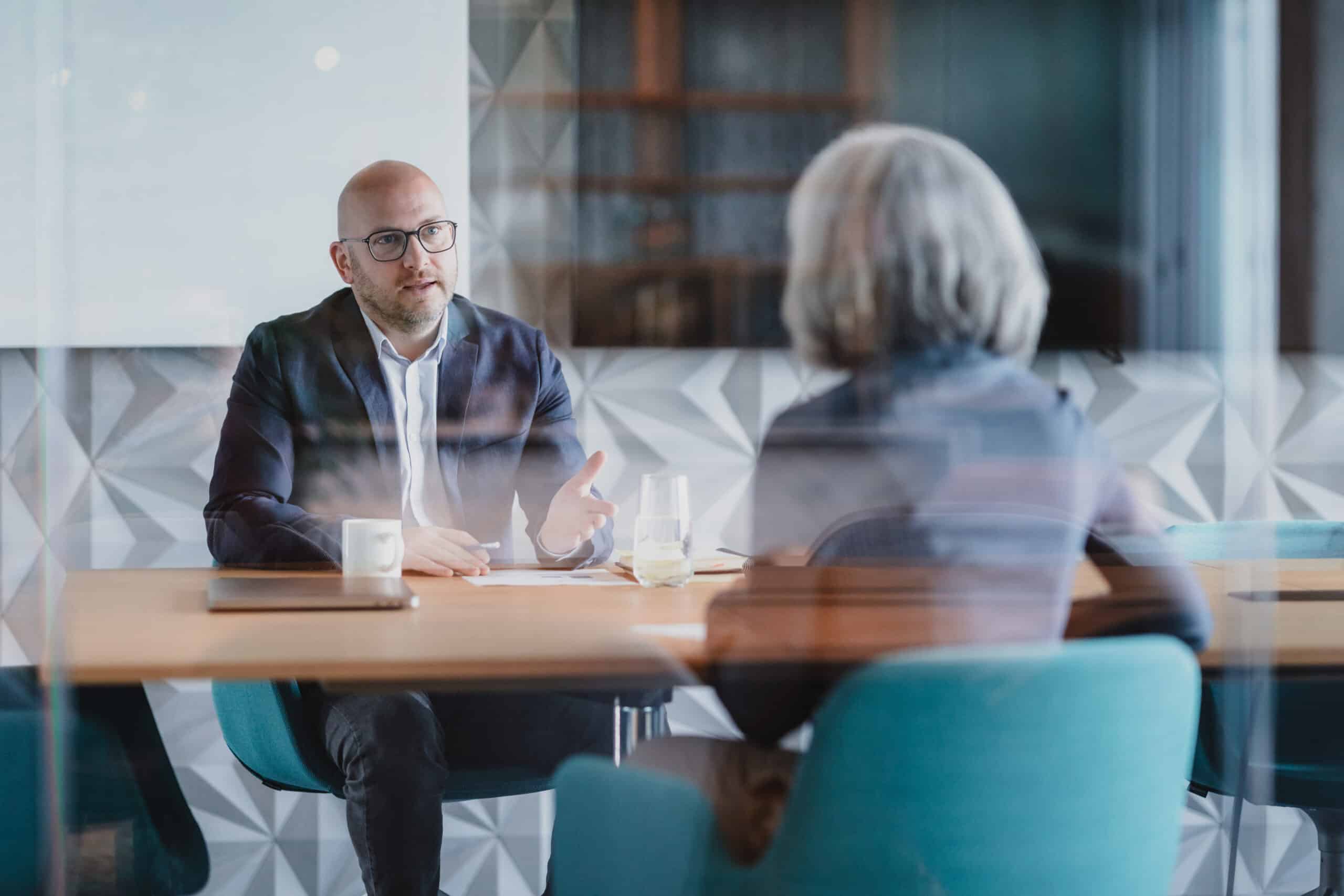 Two people discuss Leadership Development​ at a table in a modern office setting.