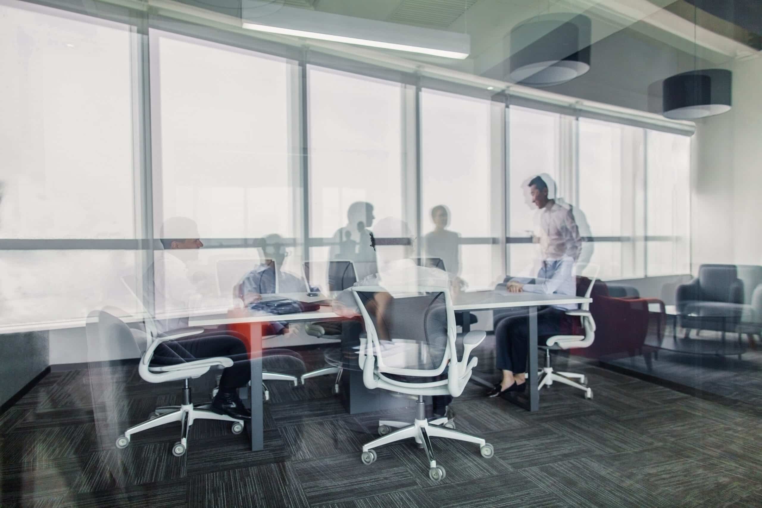 Blurry, double-exposed image of people having a meeting in a modern office.