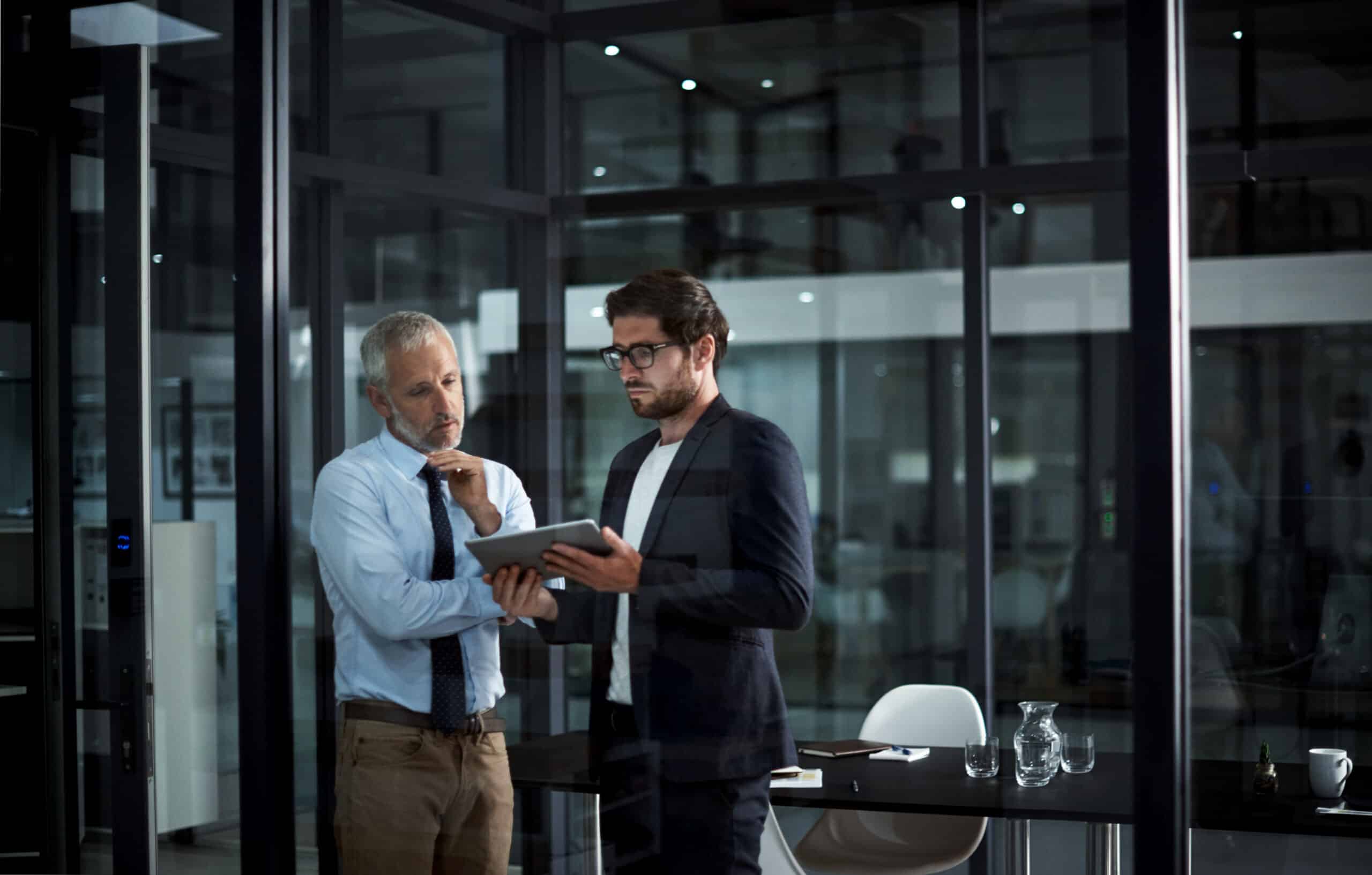 Two men in an office discuss strategies with Natural Language Processing Consulting on a tablet.