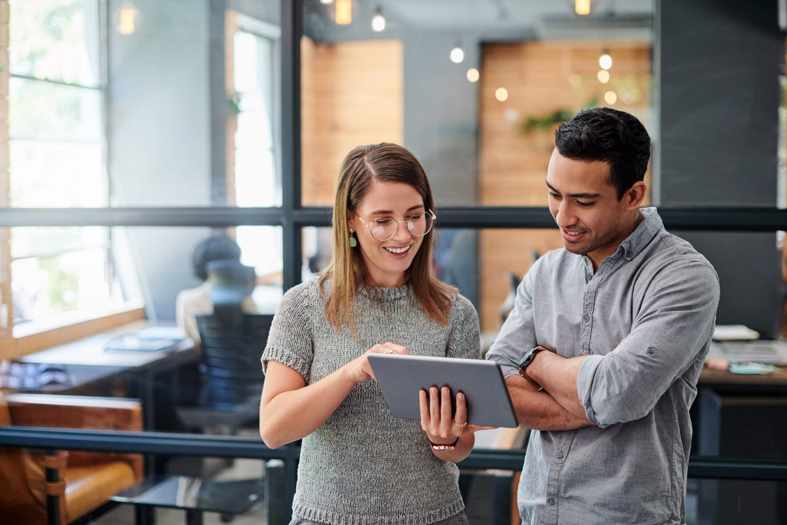 Two colleagues smiling at a tablet, discussing Cloud Migration in a modern office setting.