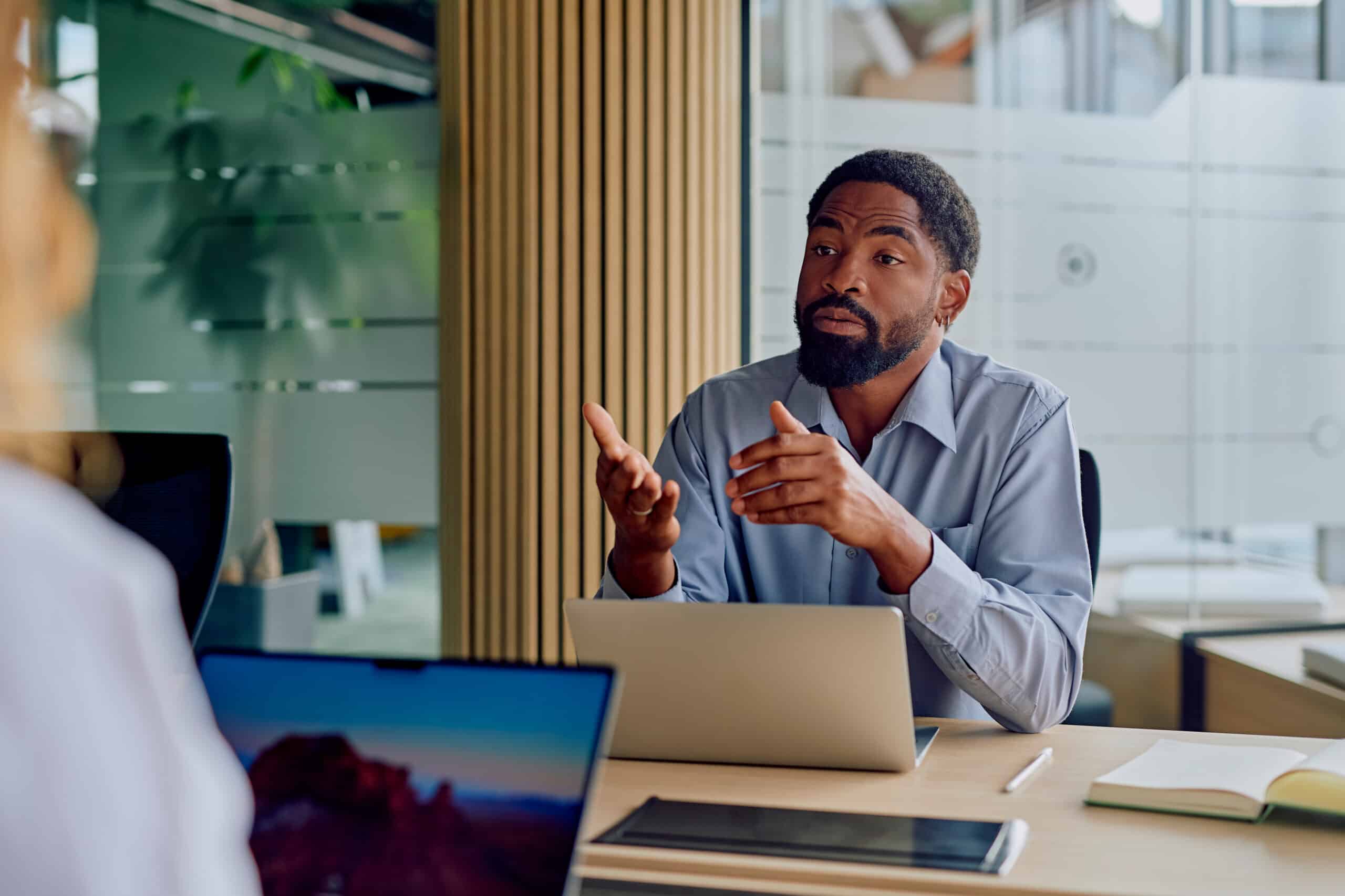 Man in an office discussing CRE Workplace Strategy during a meeting, laptop and notebook visible.