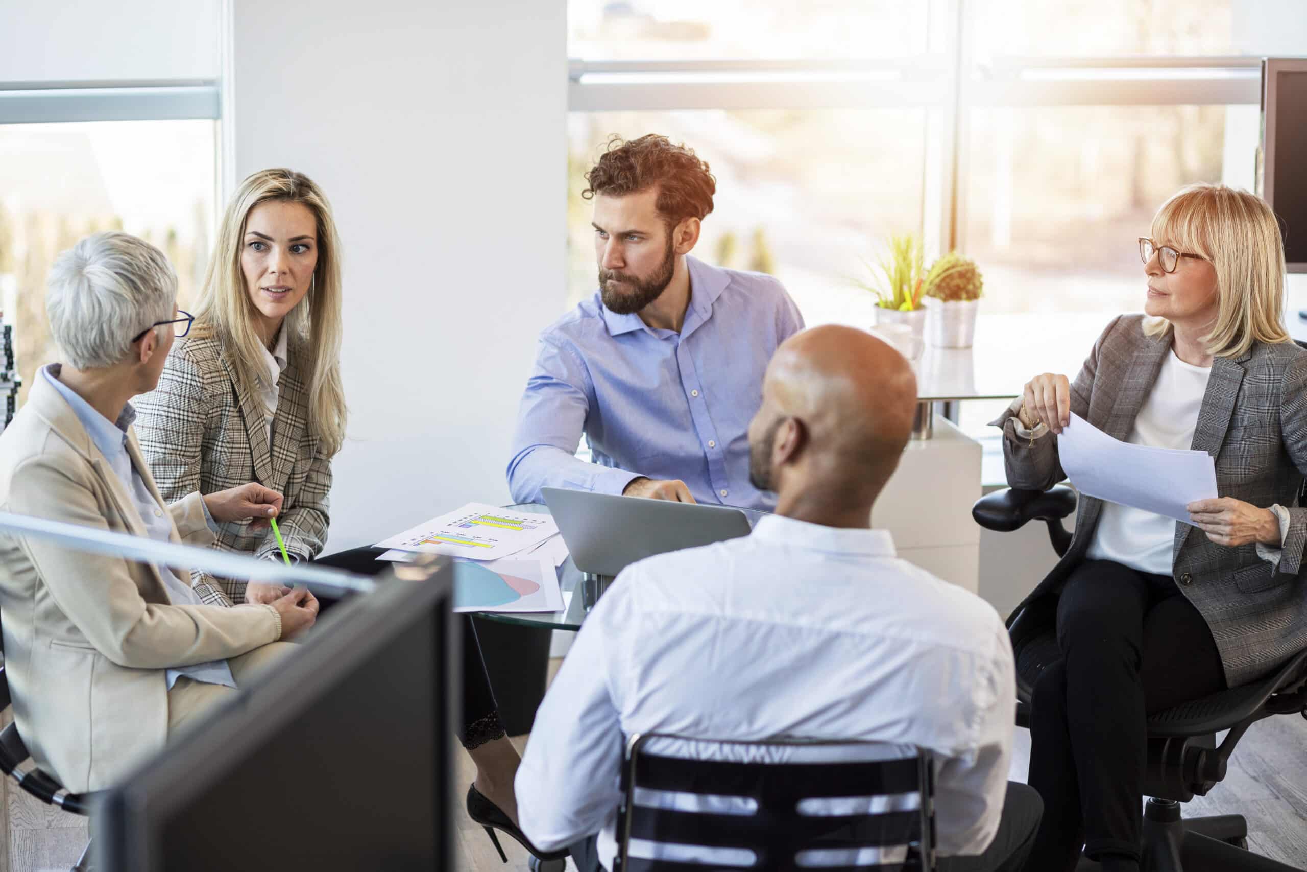 Five people discuss Expert Witness Services around a table in a bright, modern office.