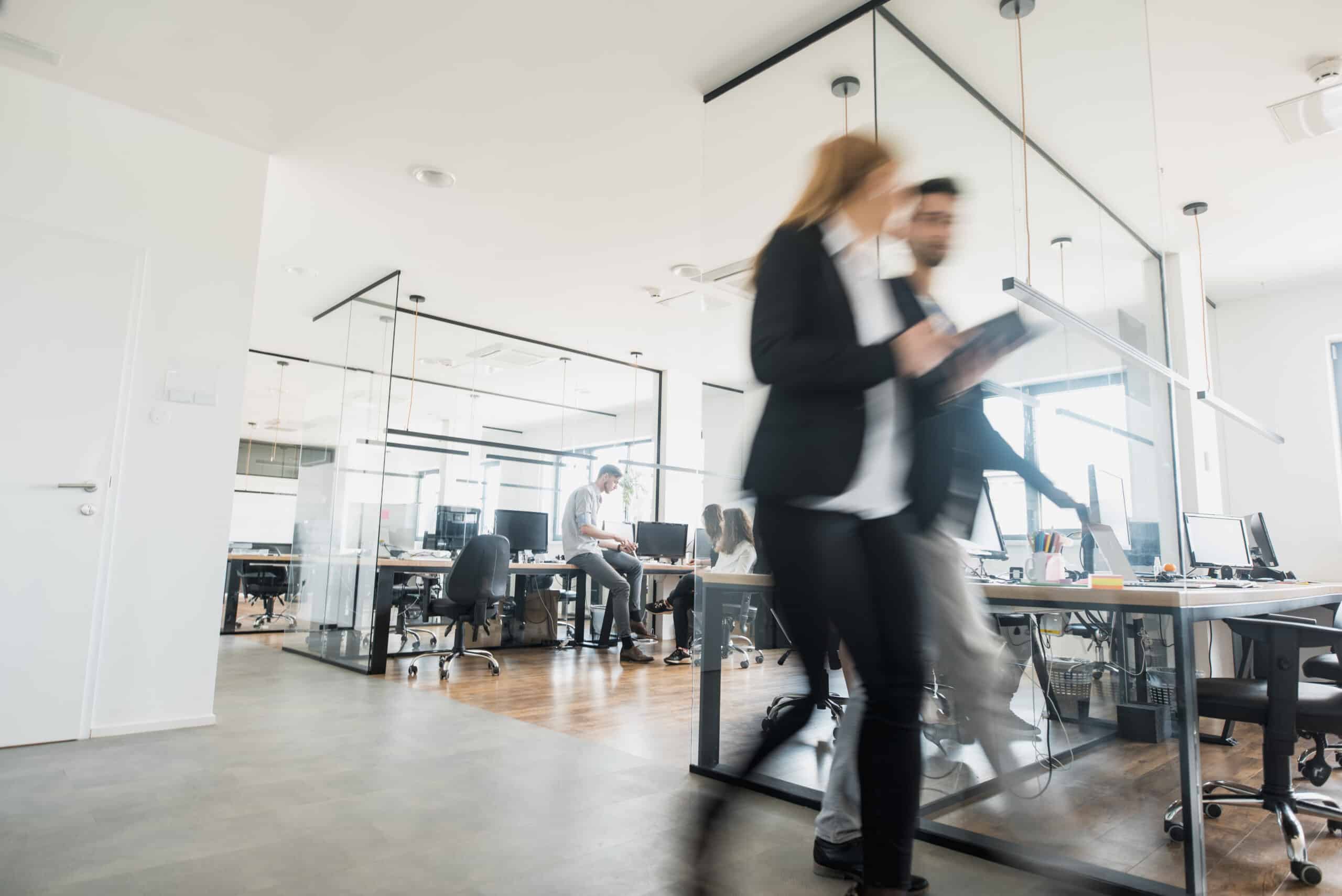 Busy modern office with Proptech Consultants working at desks and two people walking in front.
