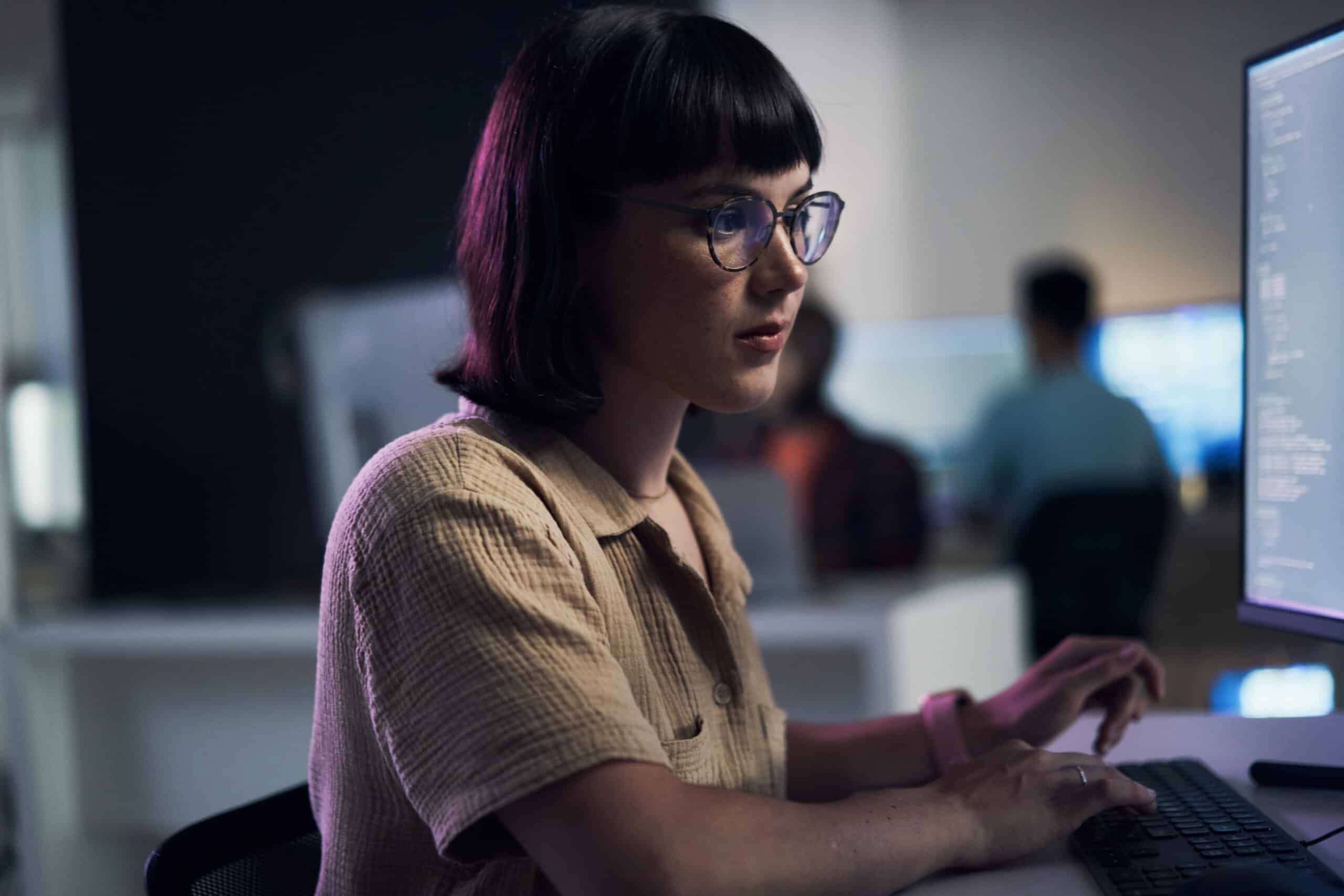 Woman with glasses working on cloud migration in an office, code visible on her screen.