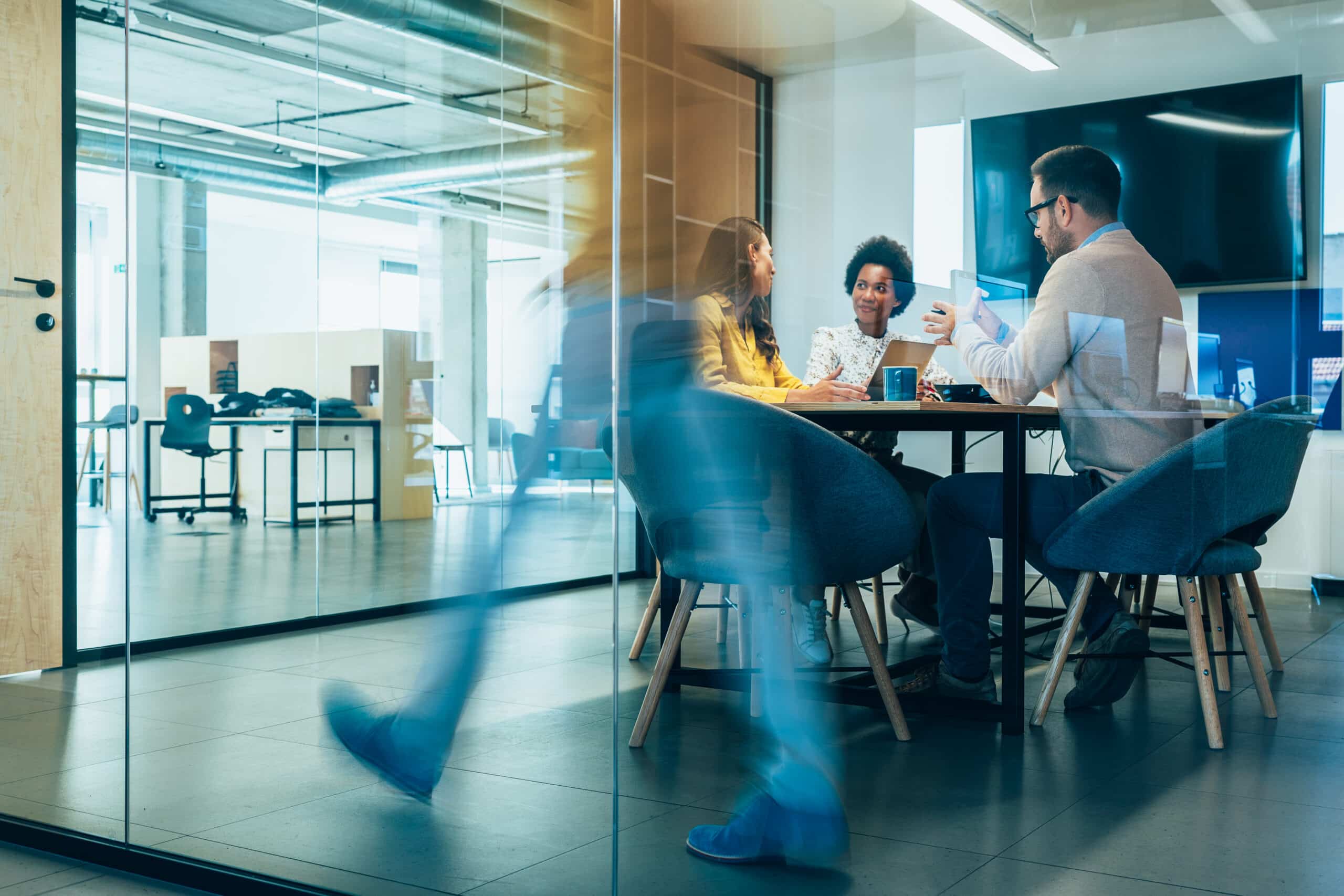 Three people discuss IT Governance as someone walks past in a modern office setting.