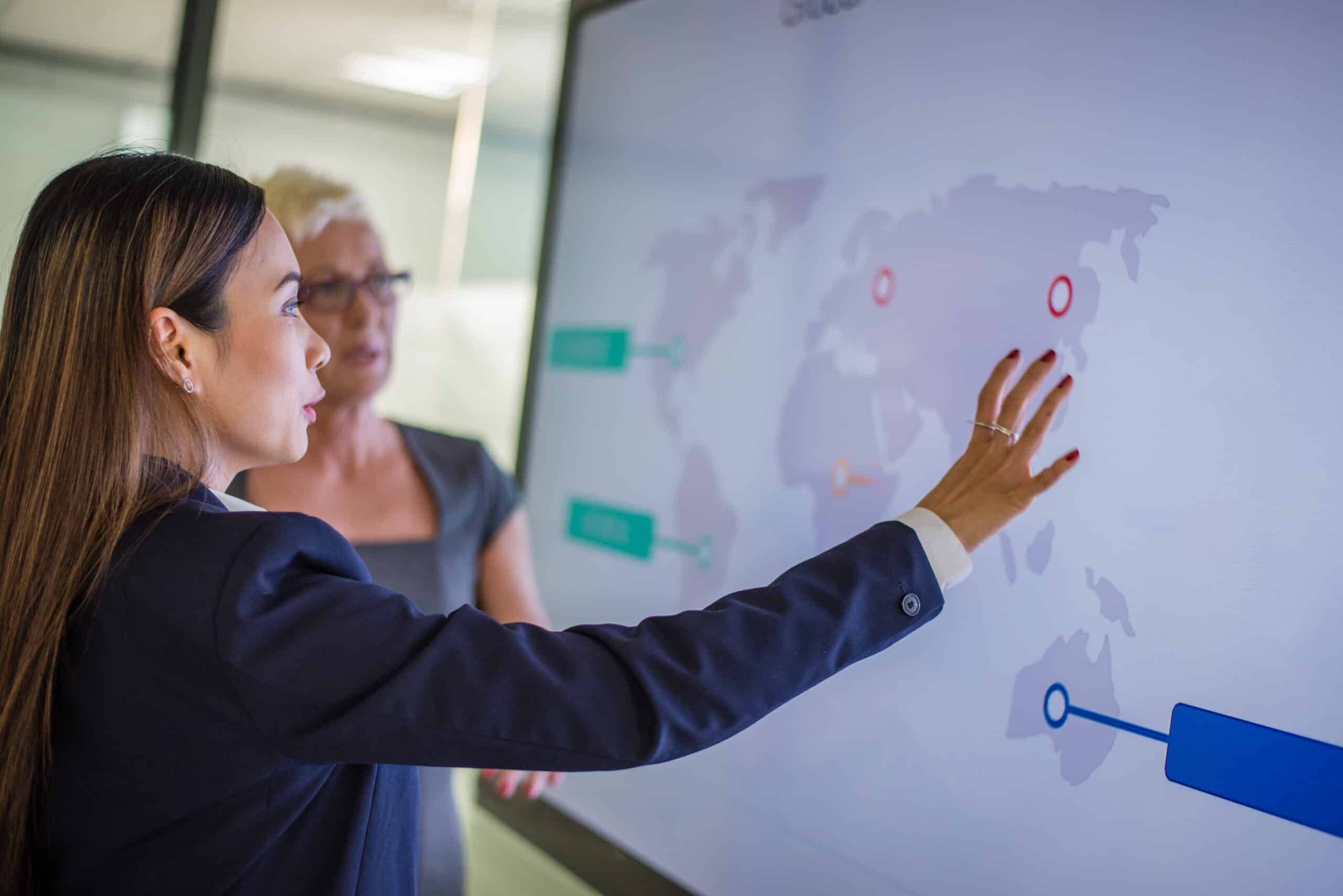 Two women discuss data on a touchscreen map during a Location Intelligence Consulting session.