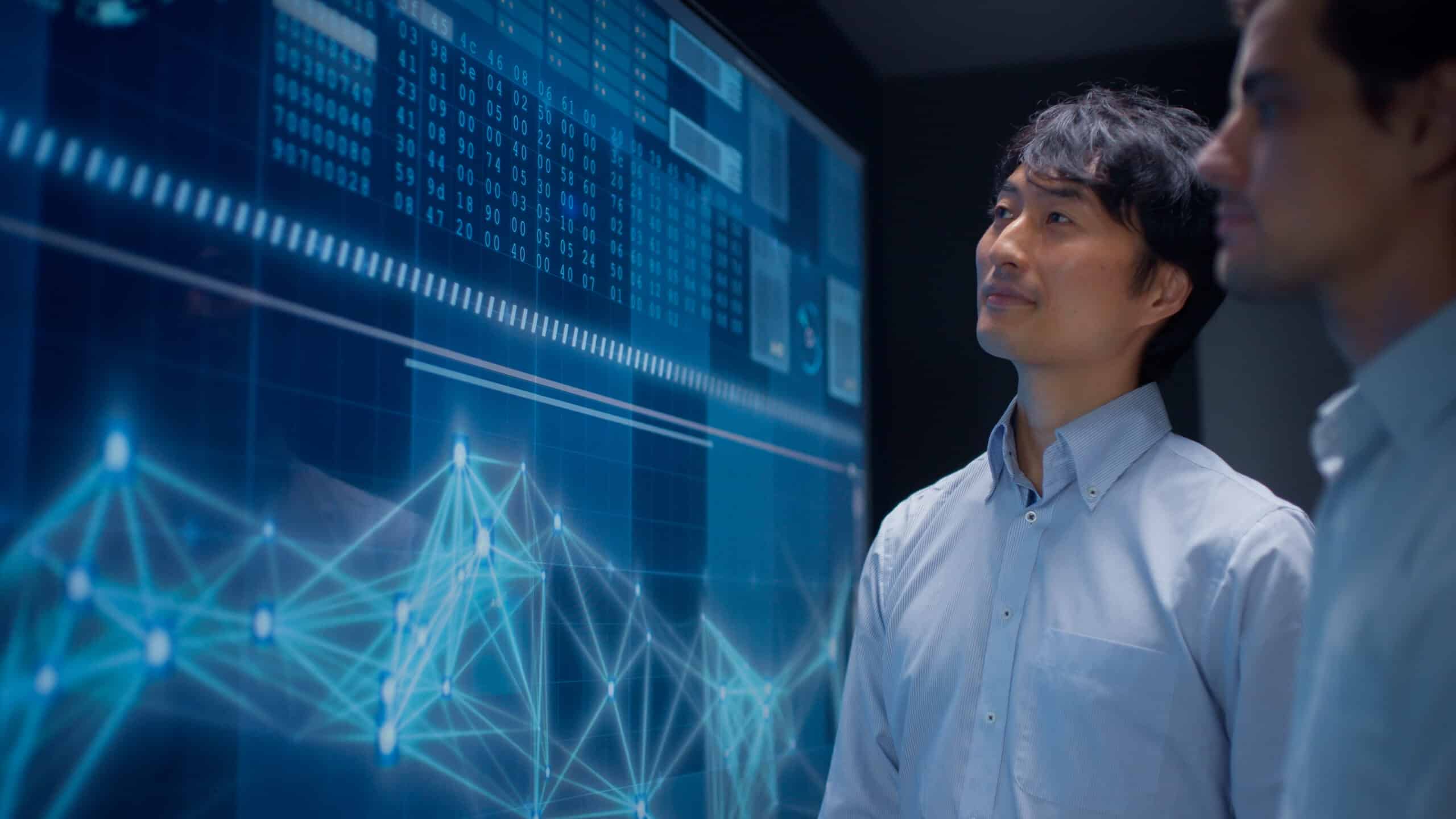 Two men review data charts on a digital screen in a Digital Twins Consulting session.