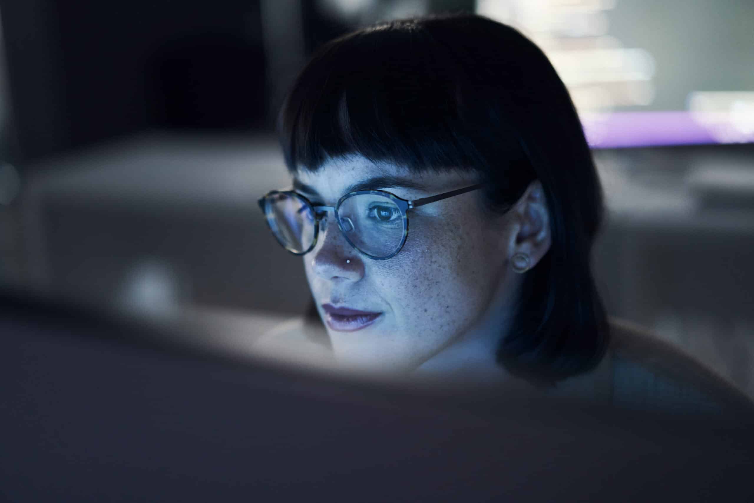 Person with glasses studies a computer screen, blue light reflecting AI Consultants at work.