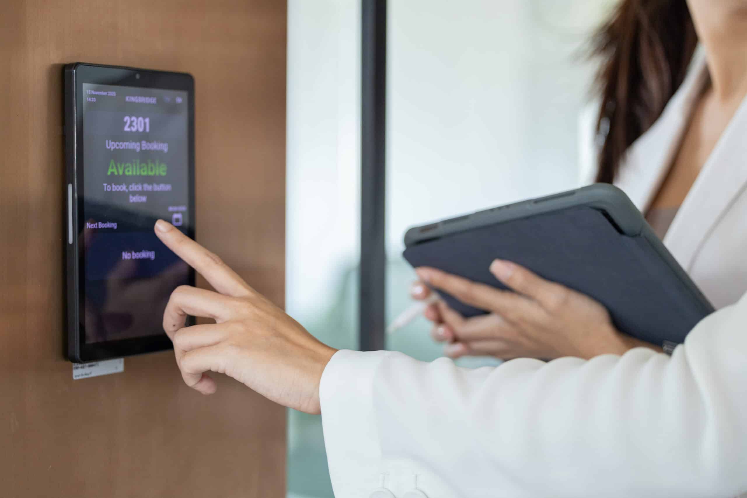 Person touches a digital booking screen while another holds a tablet nearby.