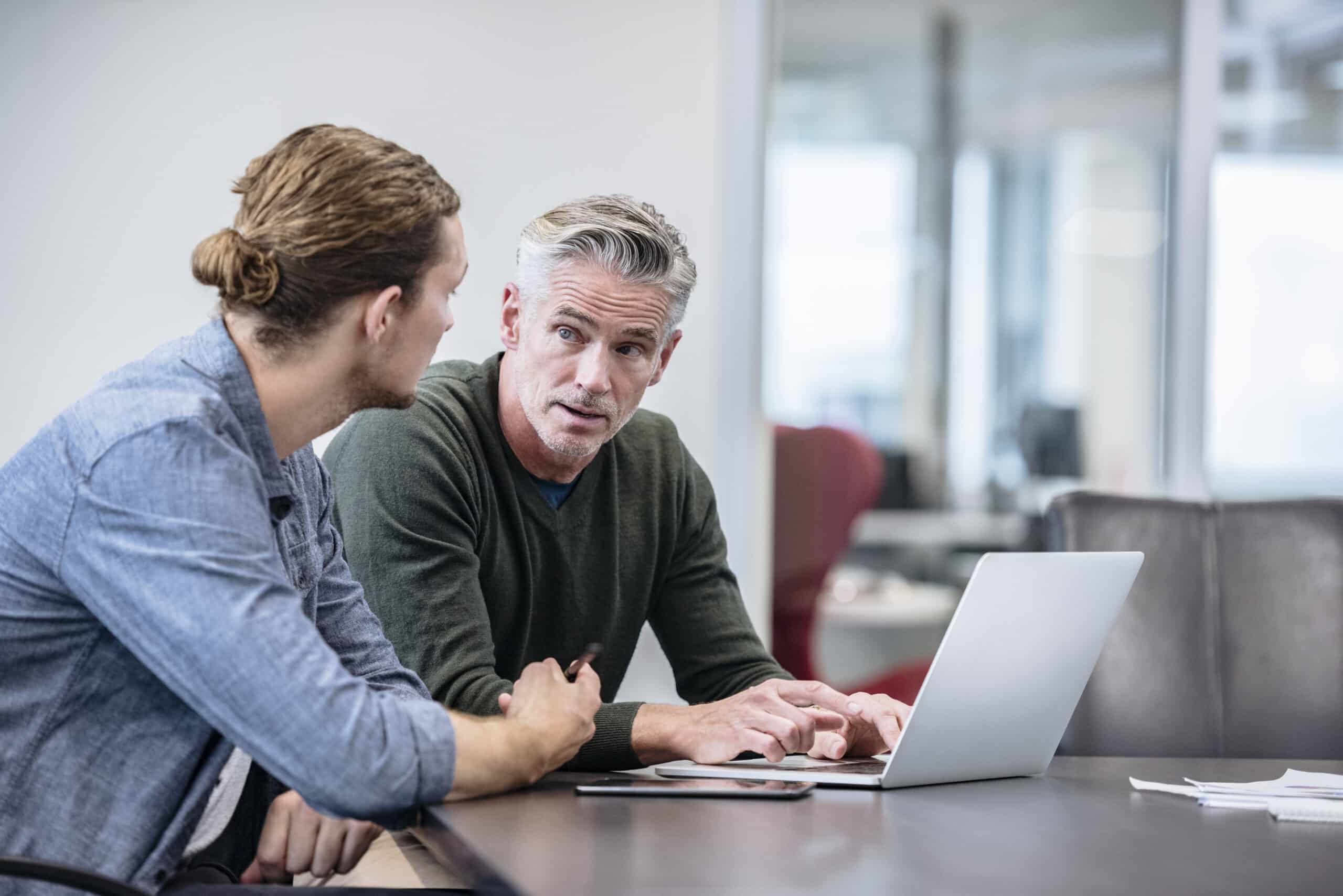 Two men discussing Proptech Consulting while working on a laptop in a modern office setting.
