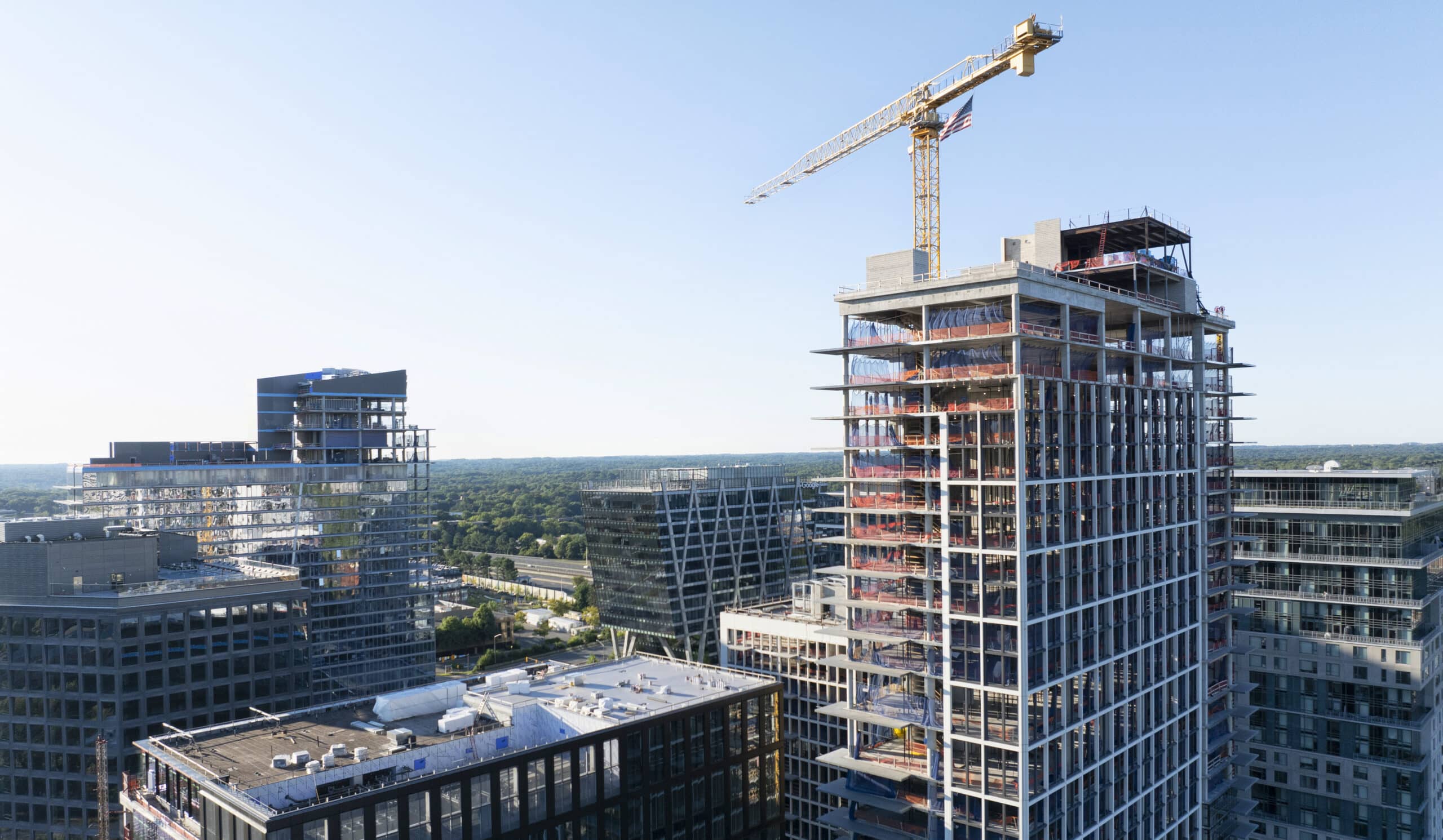 Tall building under construction with a crane, surrounded by other modern buildings.