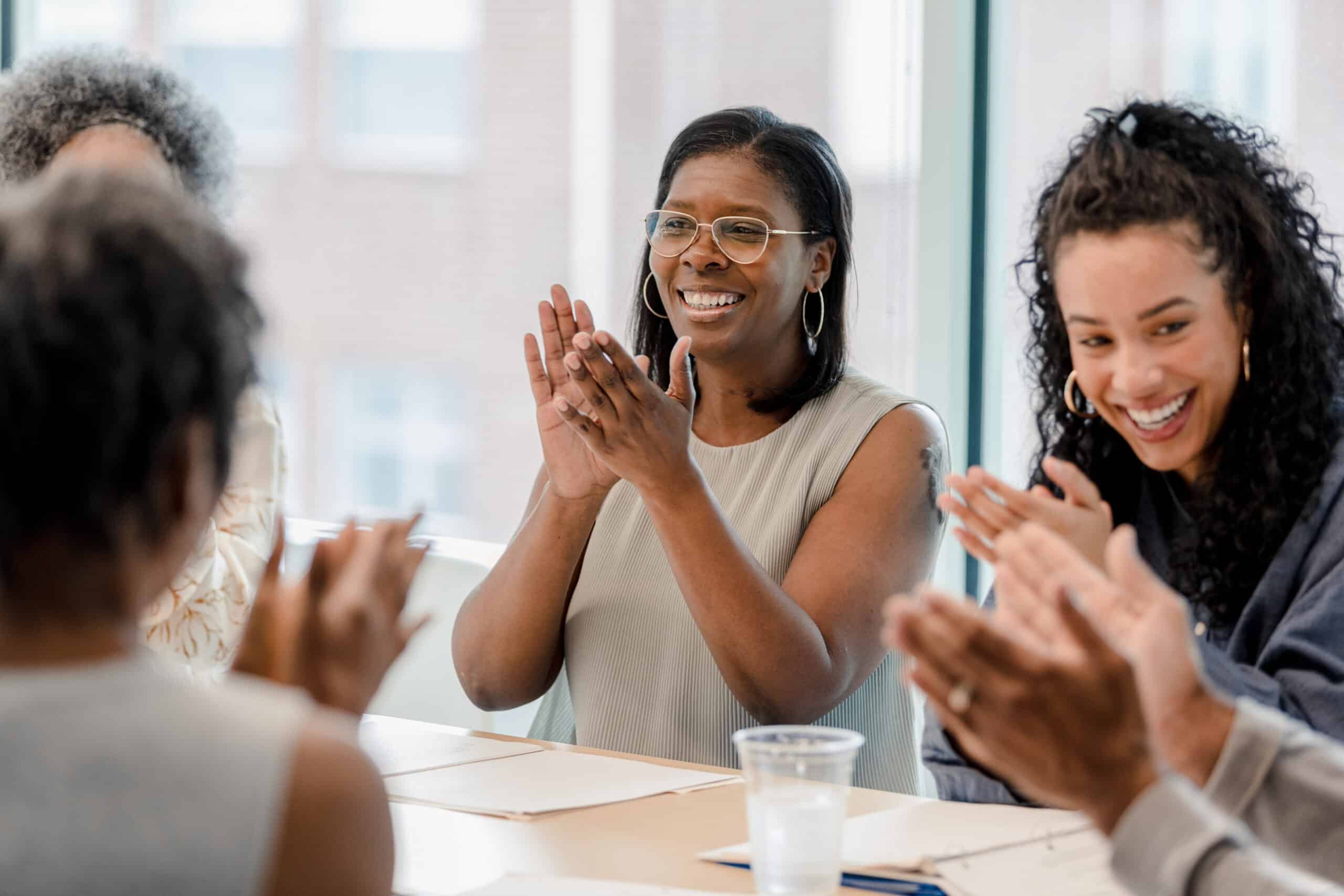People clapping and smiling in a bright office during CRE Change Management discussions.