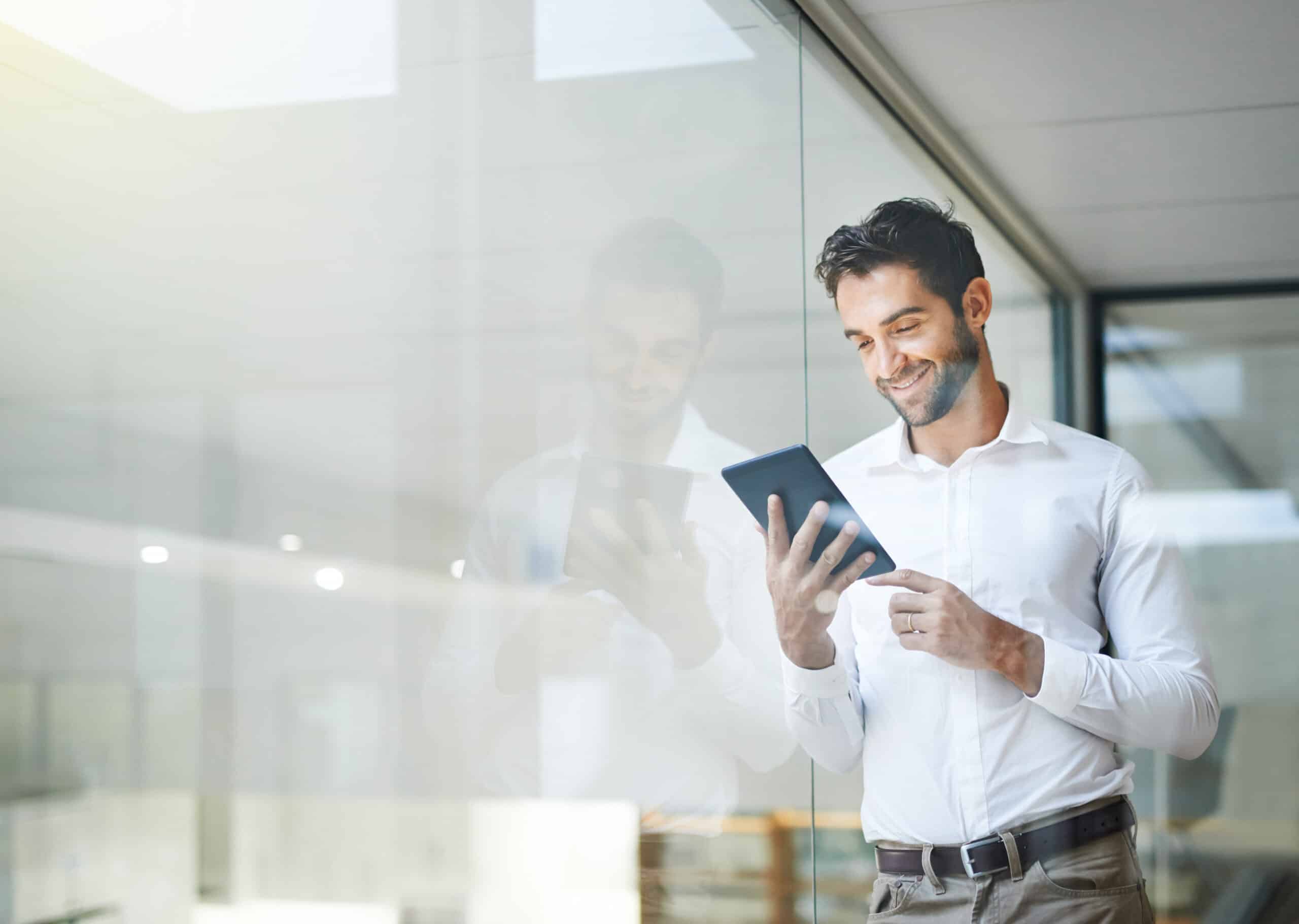 Man in white shirt smiling while using a tablet for predictive maintenance consulting in office.