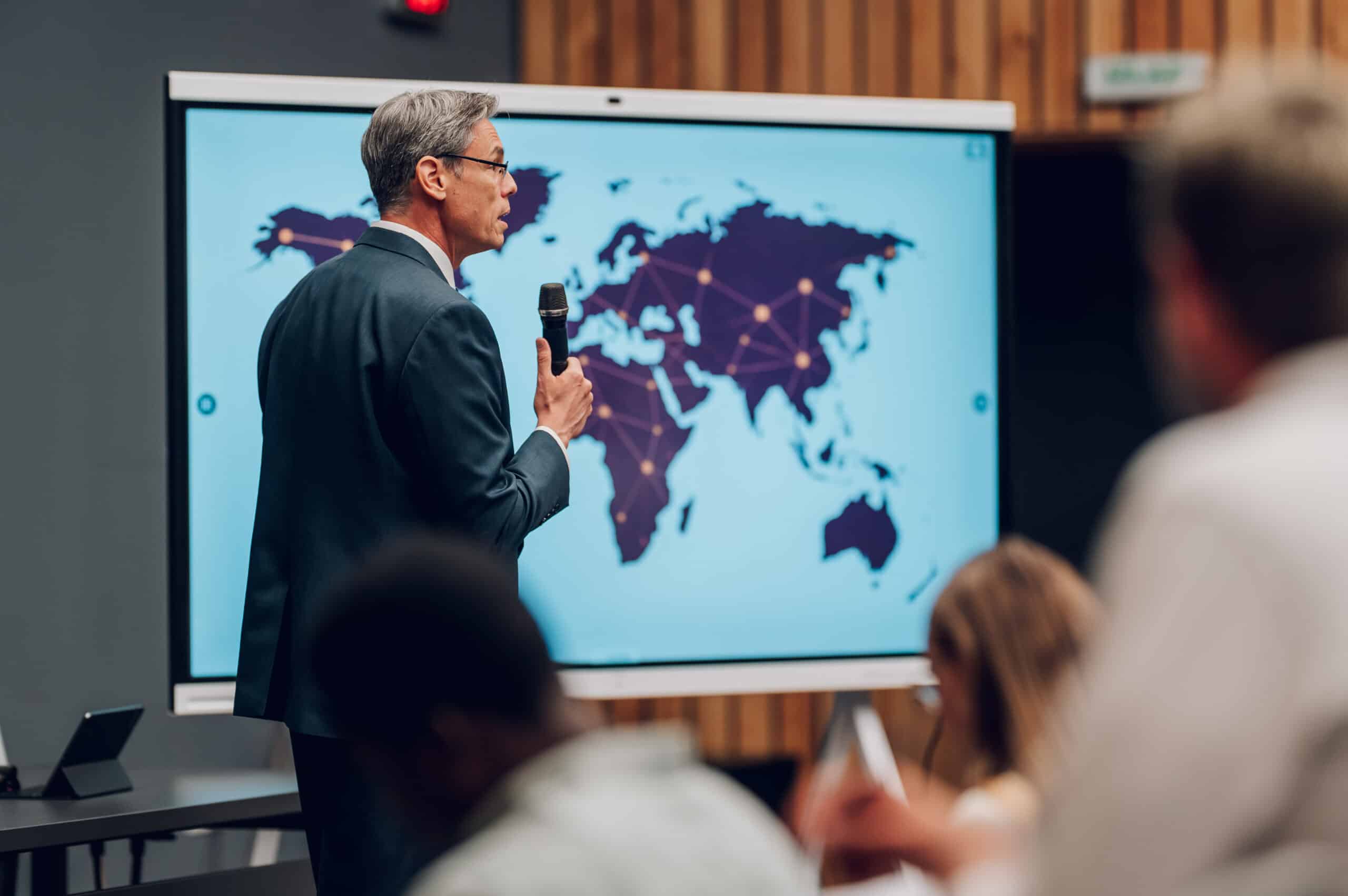 Man giving an AI Consulting presentation with a world map on screen to an audience.