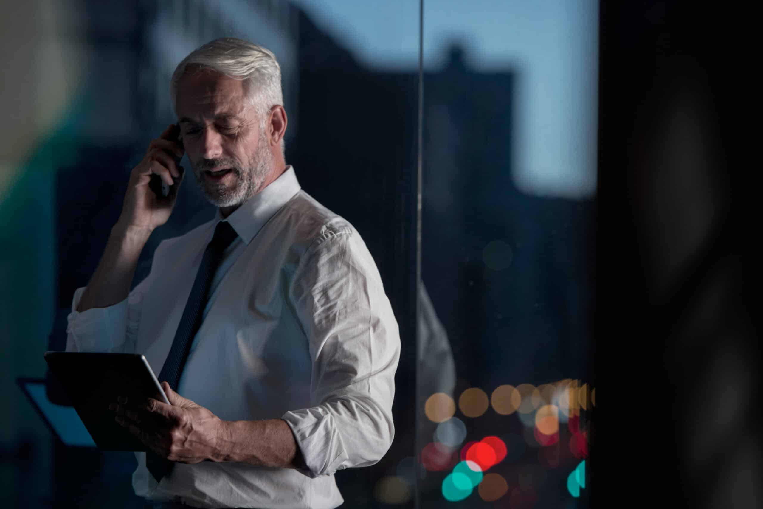 Man in dress shirt using a tablet, discussing Cloud Migration by a window at night.