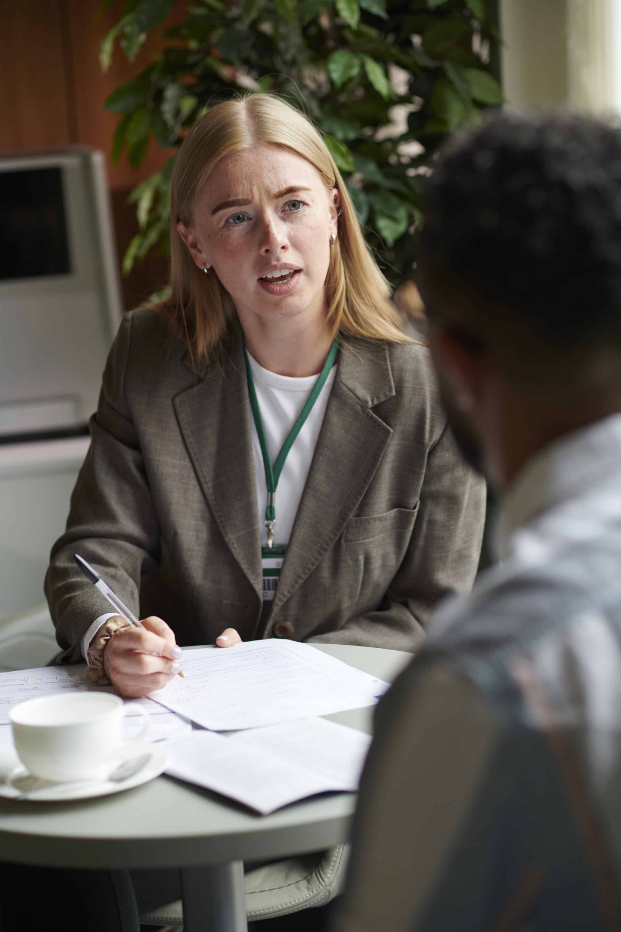 Woman in a suit talking and writing notes during a meeting at a table with another person.