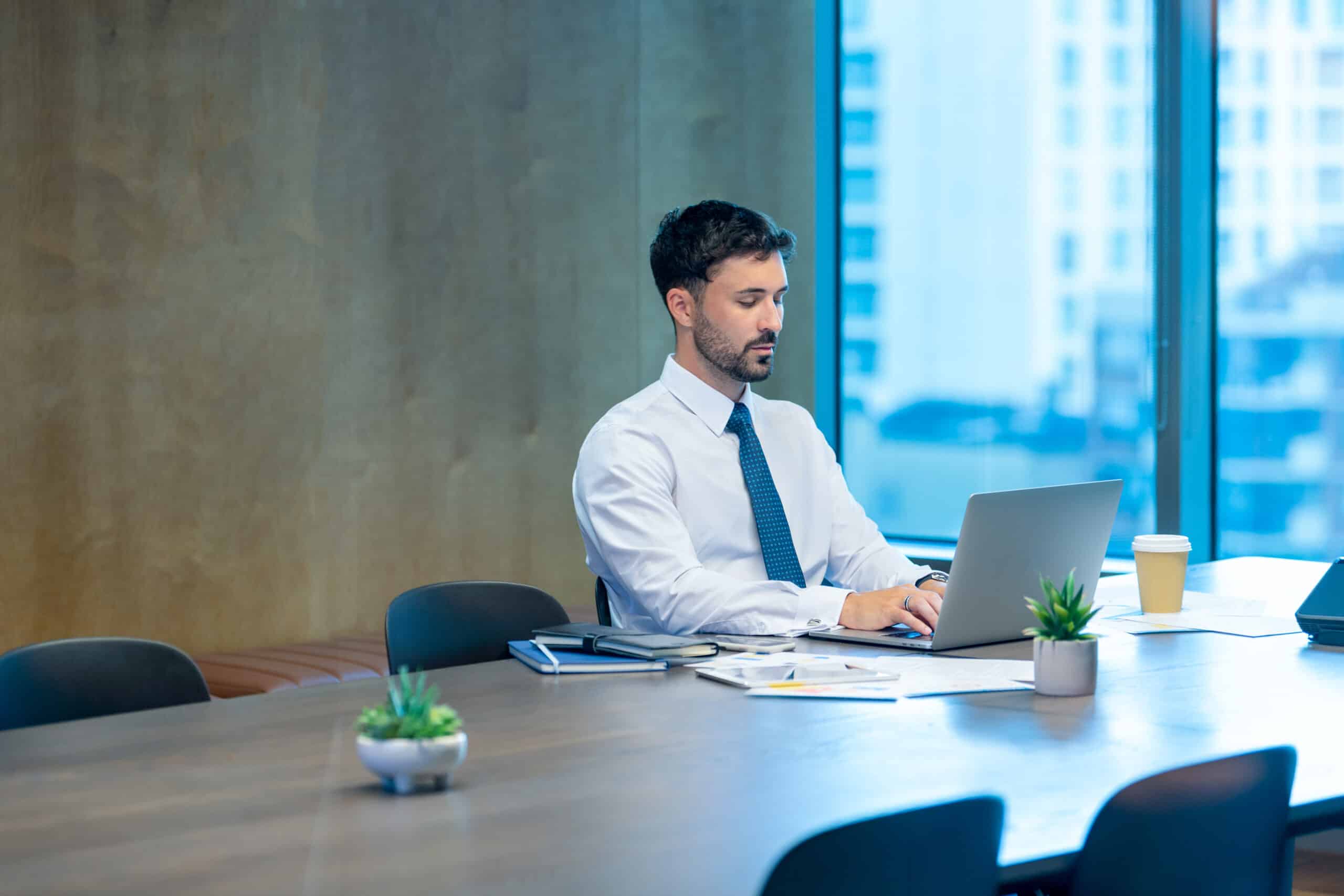 Man in business attire working on IT Architecture consulting at a conference table with laptop.