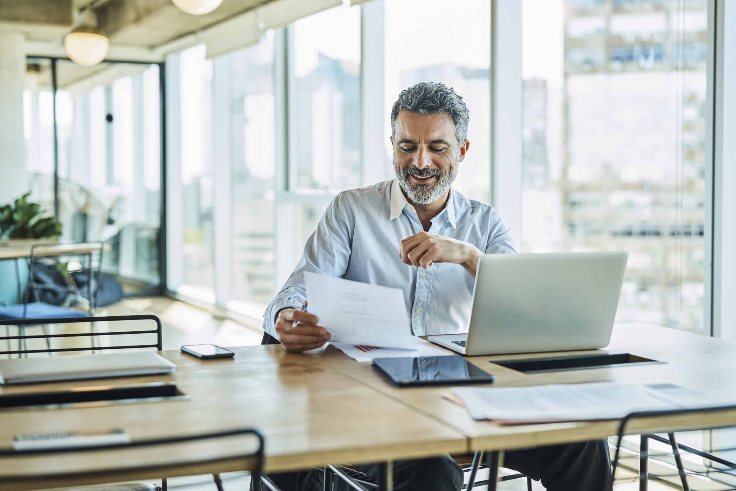 Smiling man reading a document at his desk, exploring Digital Twins Consulting in a modern office.