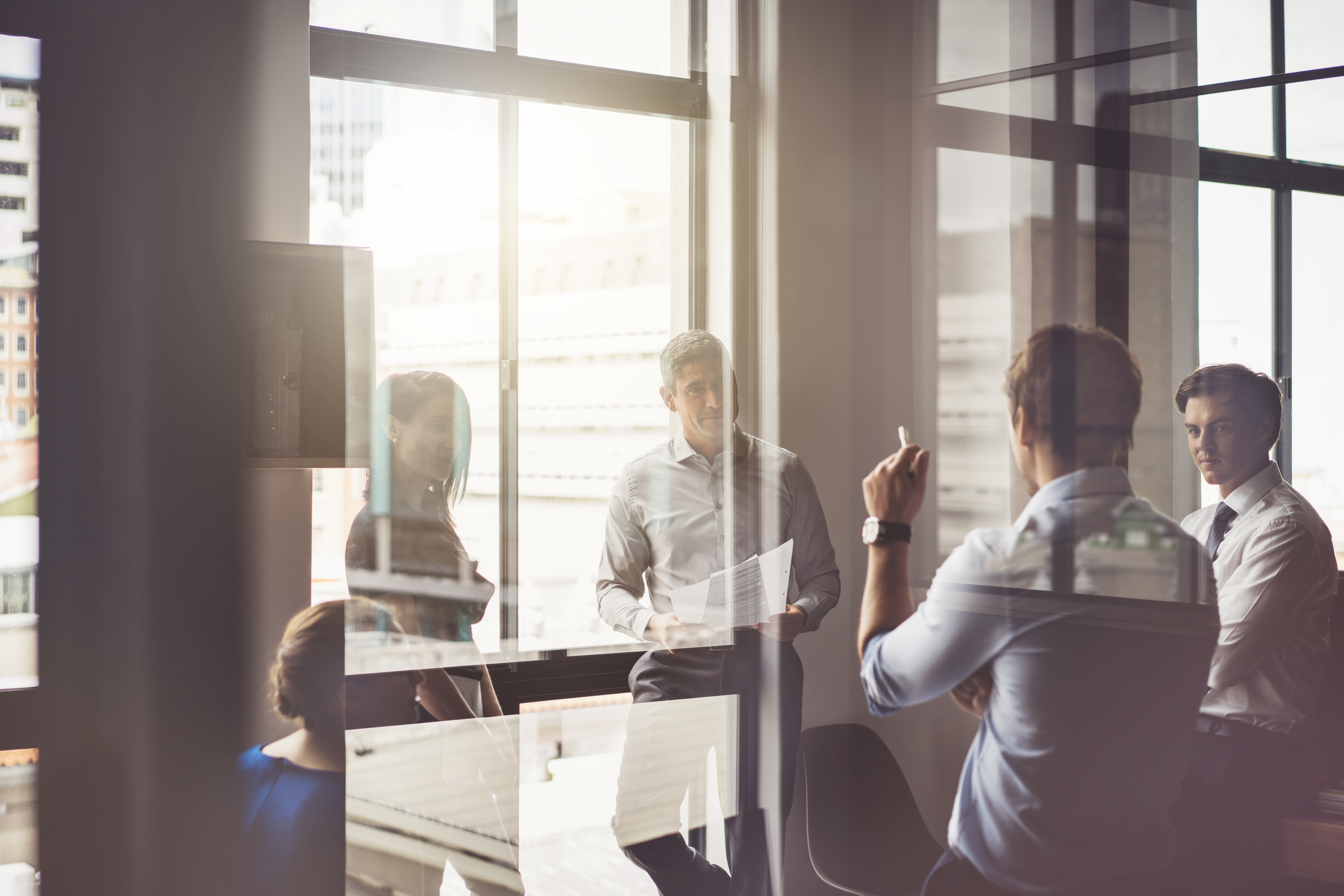 Four people discuss CRE Workplace Strategy in a modern office with large windows and reflections.