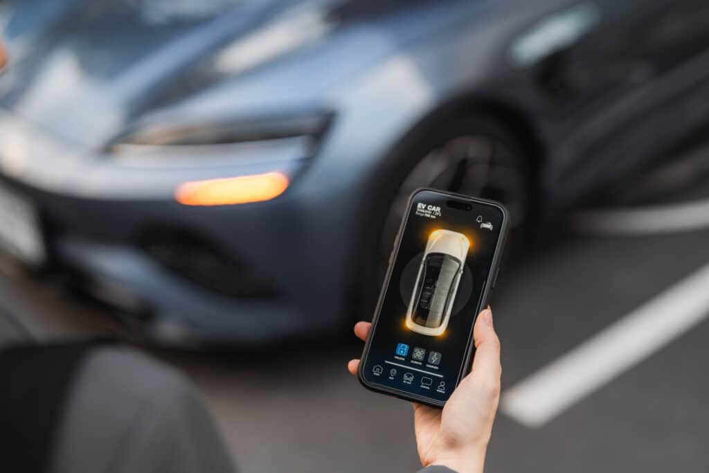 Person holding smartphone with car control app displayed in front of a blurred parked car.