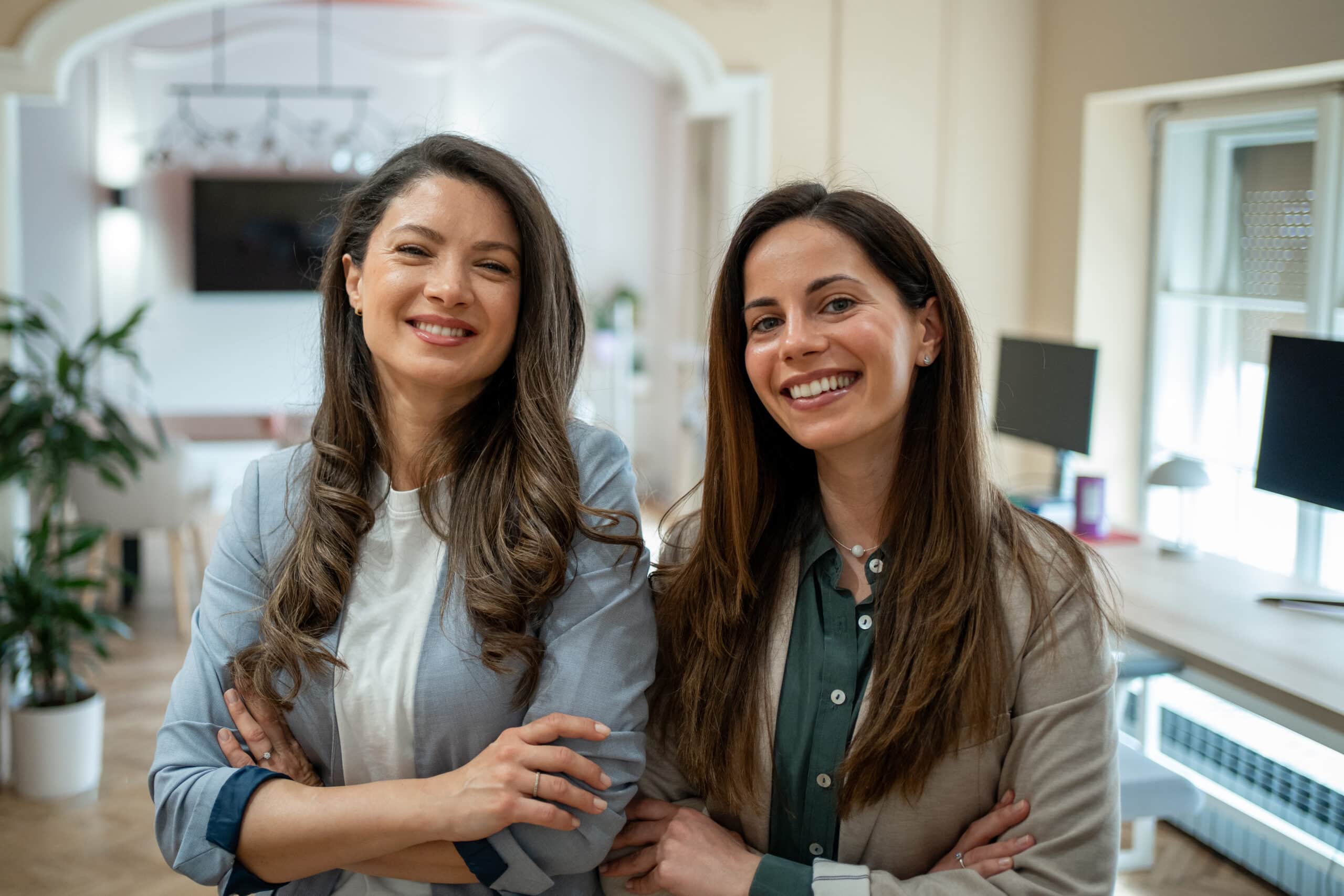 Two women smiling with arms crossed in a bright office, experts in employee retention consulting.