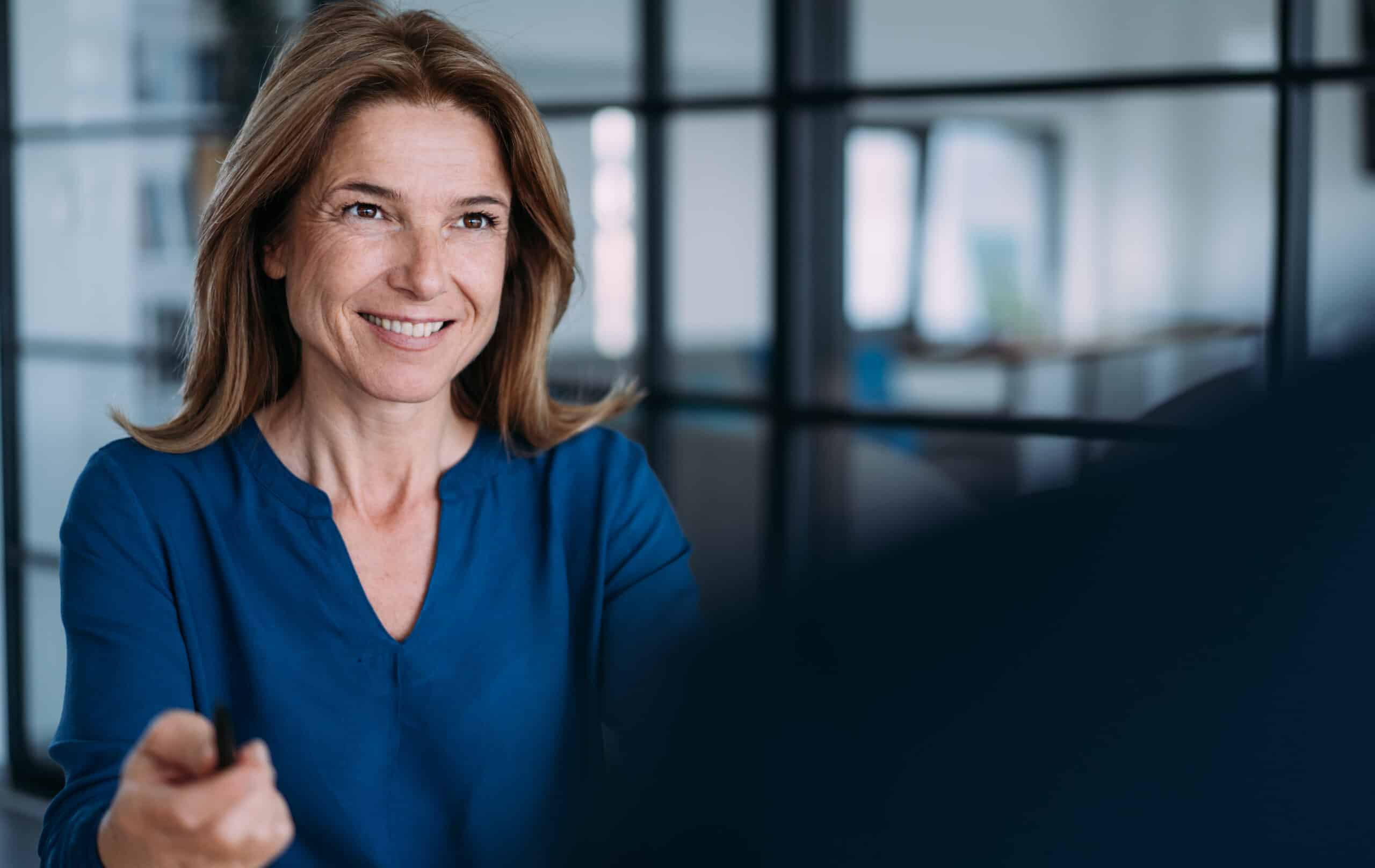 Smiling woman in blue blouse indoors, offering a pen—professional employer branding consulting.