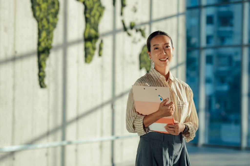 Woman smiling and holding folders, standing indoors—perfect for growth strategy consulting firms.