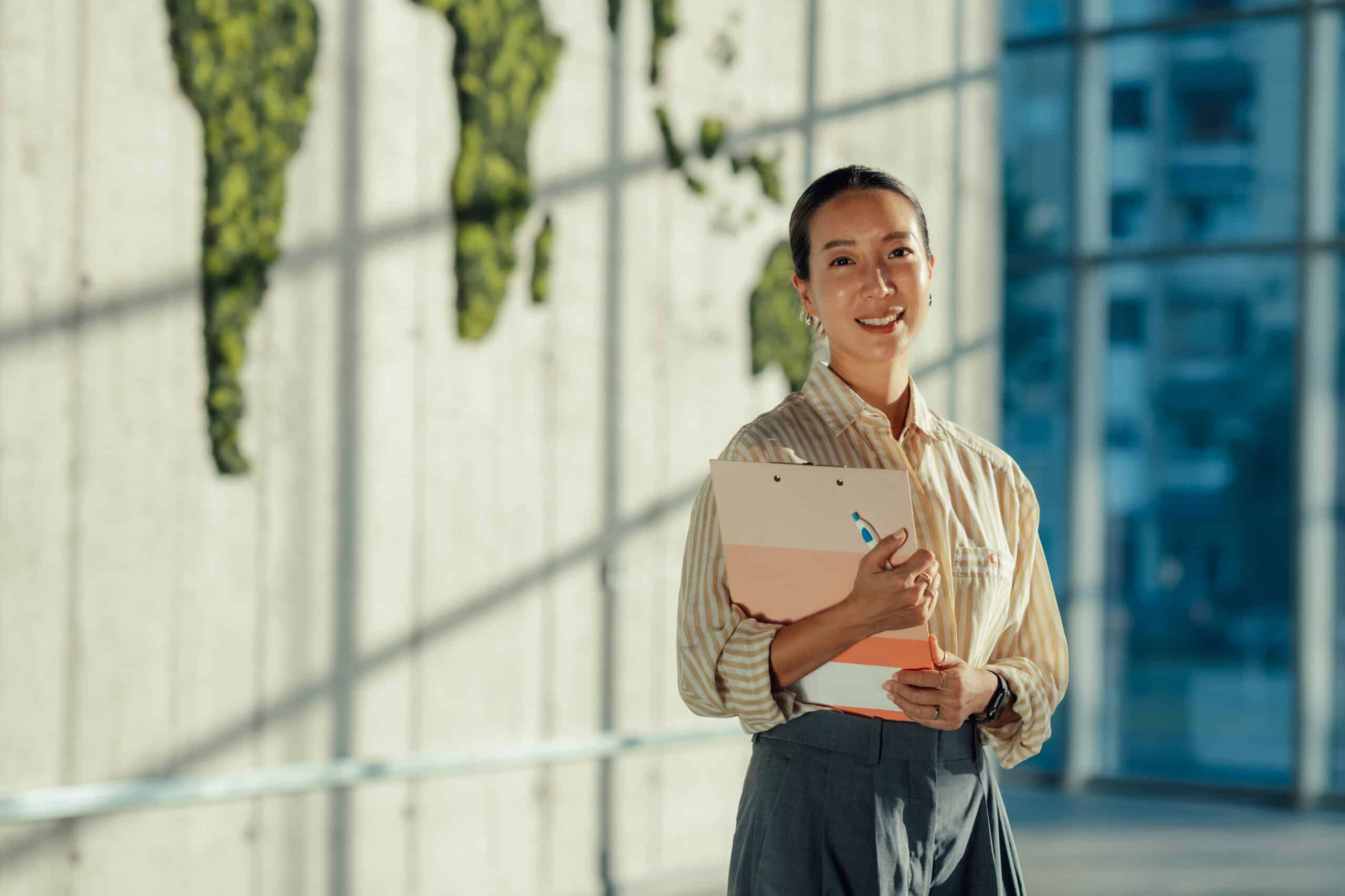 Woman smiling and holding folders, standing indoors—perfect for growth strategy consulting firms.