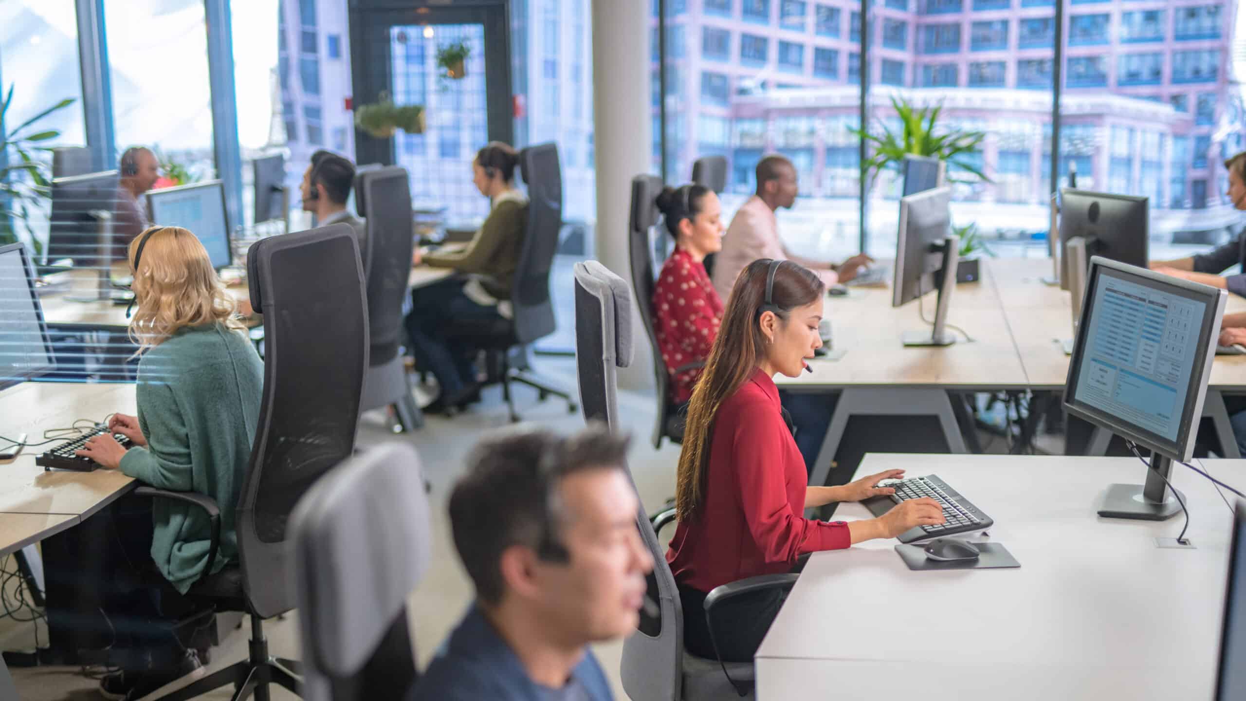 People working at computers in a modern, bright outsourcing consulting office with large windows.