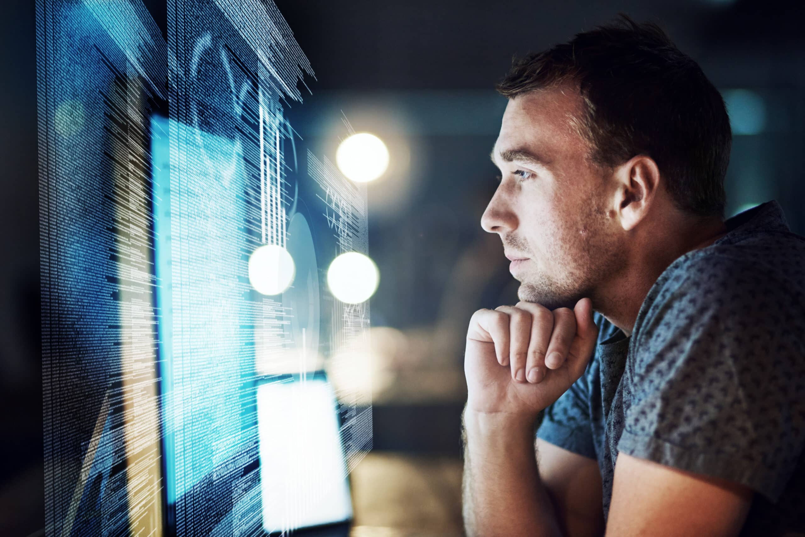 Man intently looking at computer screens, reflecting code, data graphics, and tech talent consulting.