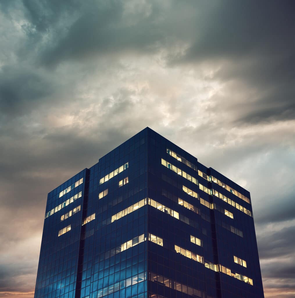 Glass office building at dusk lit up under dramatic clouds, ideal for CRE Underwriting analysis.