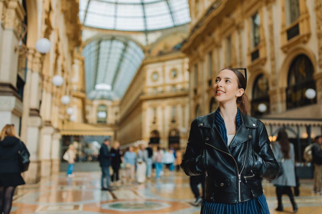 Woman in black leather jacket smiles in a grand arcade, exuding Luxury Brand Governance style.