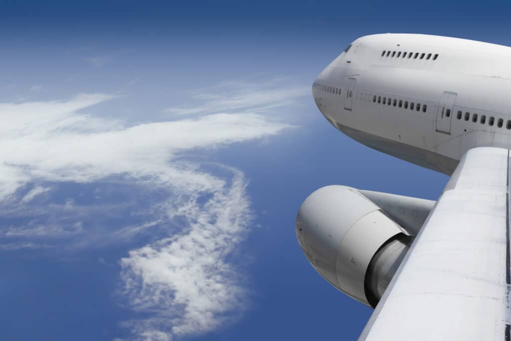 View of an airplane wing above clouds, pondering: Who pays for aviation’s decarbonization?.