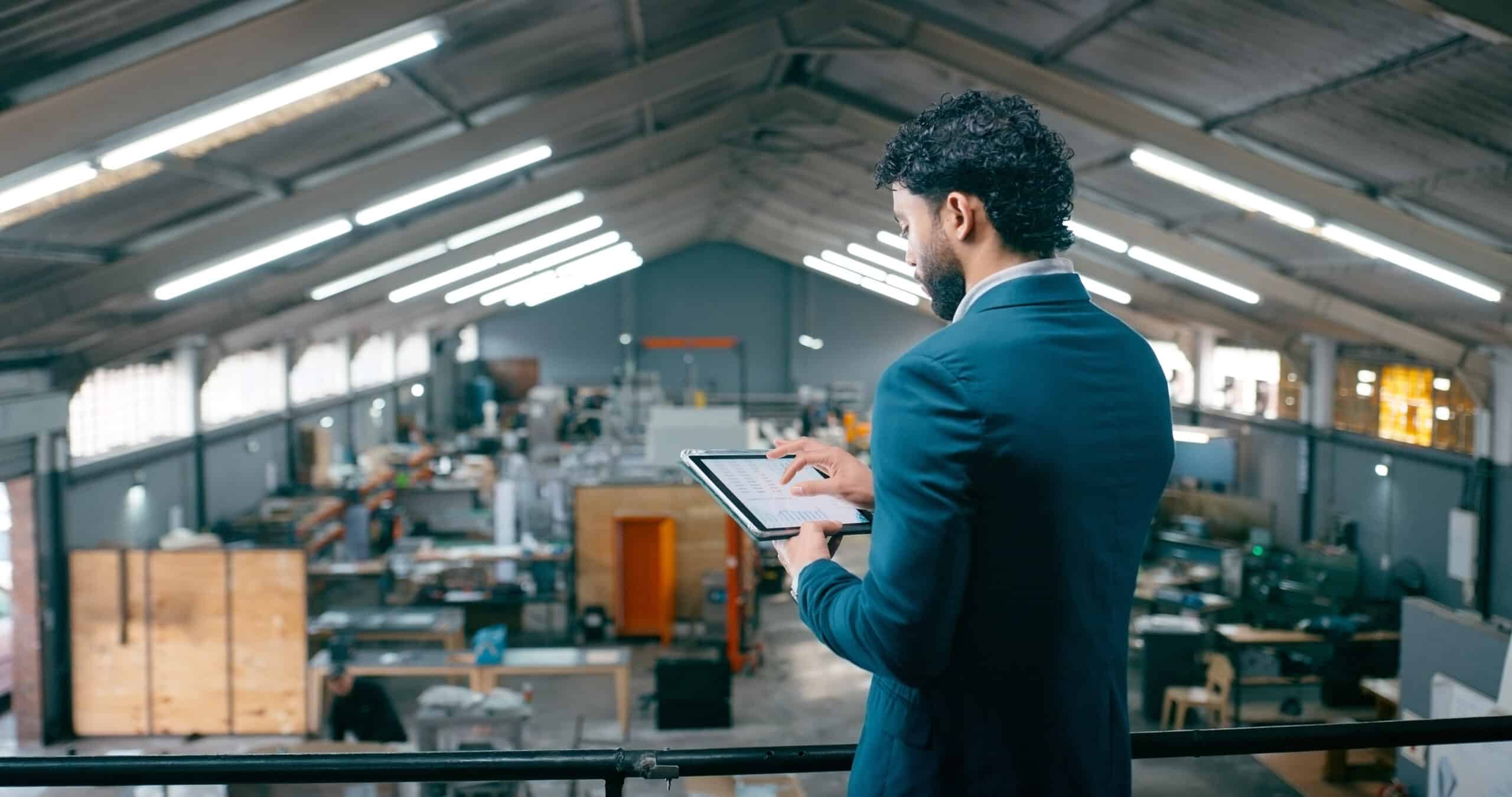 Man in suit uses tablet, overseeing warehouse operations with aps consulting expertise.