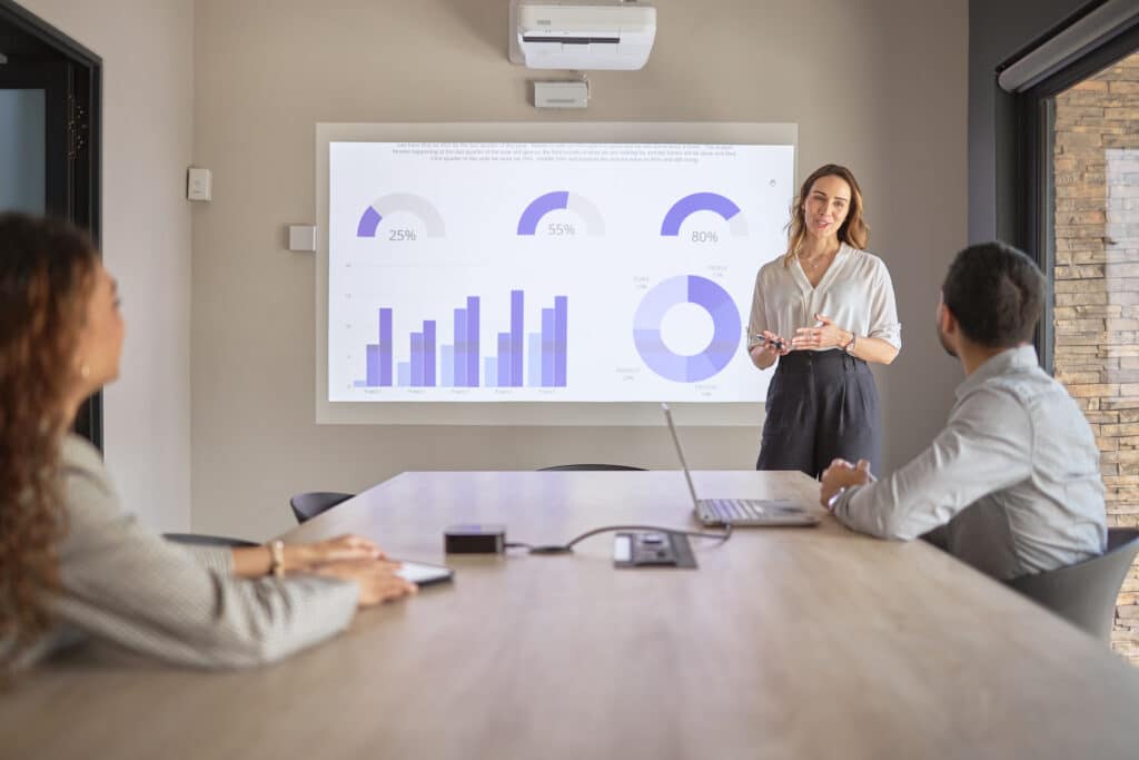 Woman presenting graphs on Capital Project Management Consulting to two people in a meeting room.
