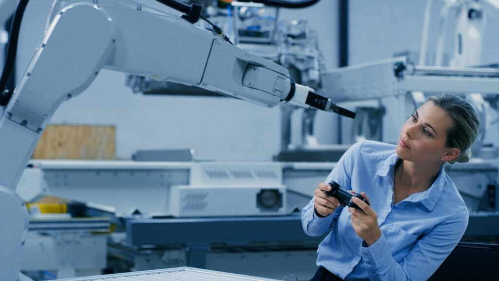 Woman using remote control and computer vision consulting to operate a robotic arm in industry.