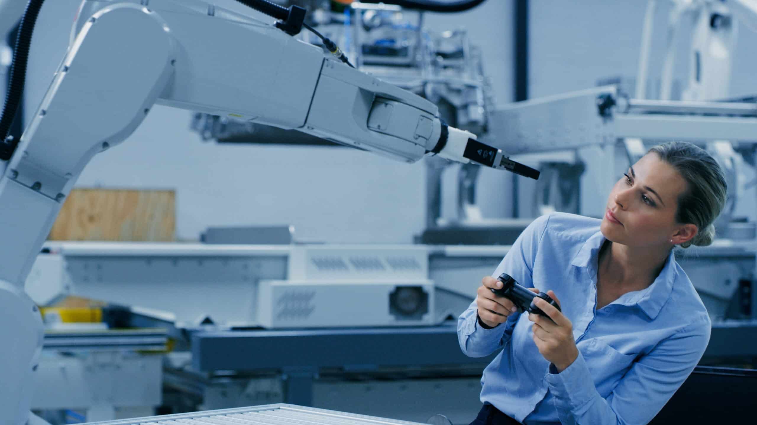 Woman using remote control and computer vision consulting to operate a robotic arm in industry.