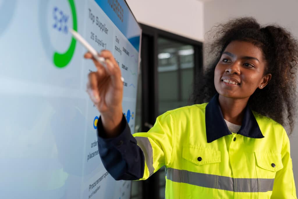 Woman in high-visibility jacket points at a data chart during manufacturing analytics consulting.